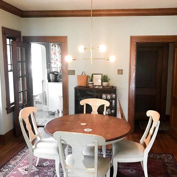 Art Deco chandelier with exposed bulbs and brass finish hanging above round wooden dining table with white chairs. - CHANDELIER MODEL NO. 5598