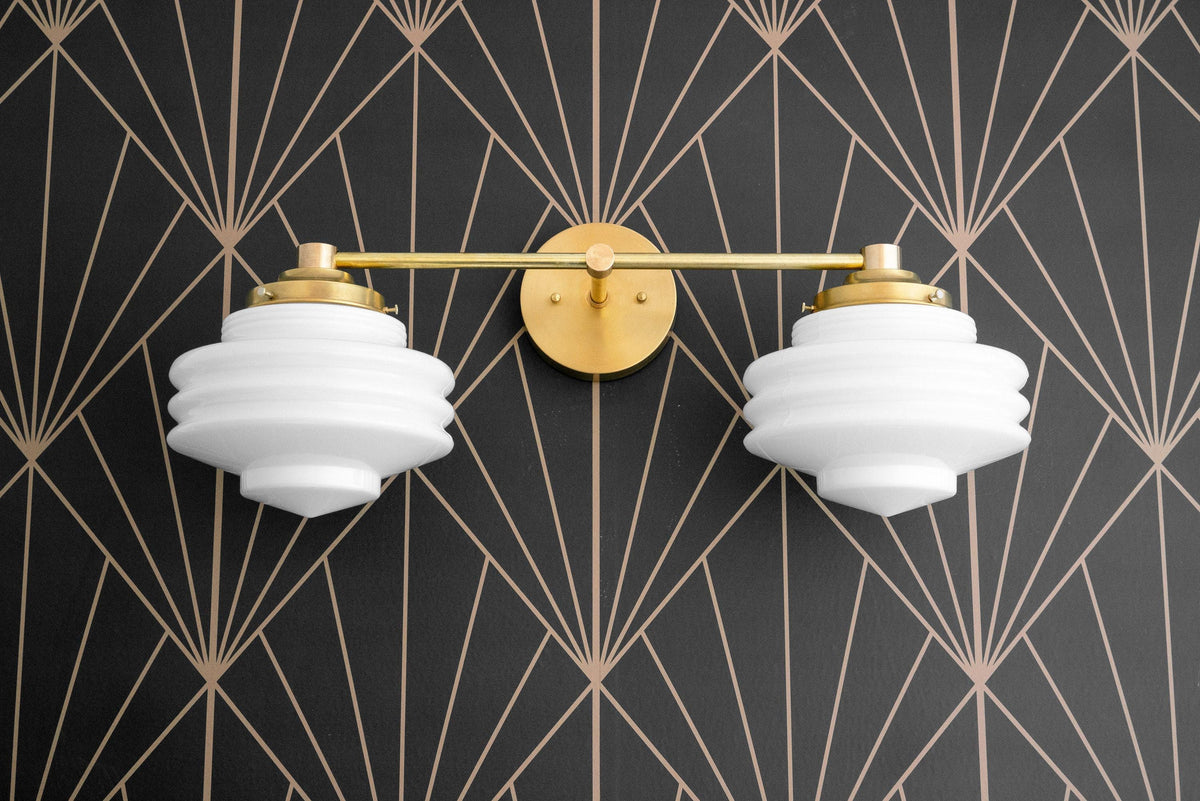 Two-bulb vanity light in polished brass with white globe shades against black and gold geometric wallpaper. - VANITY LIGHT MODEL NO. 9479