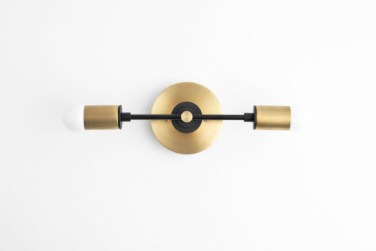 Art Deco vanity light with black metal arms and raw brass cylindrical shades mounted on a round brass backplate. - VANITY LIGHT MODEL NO. 8057