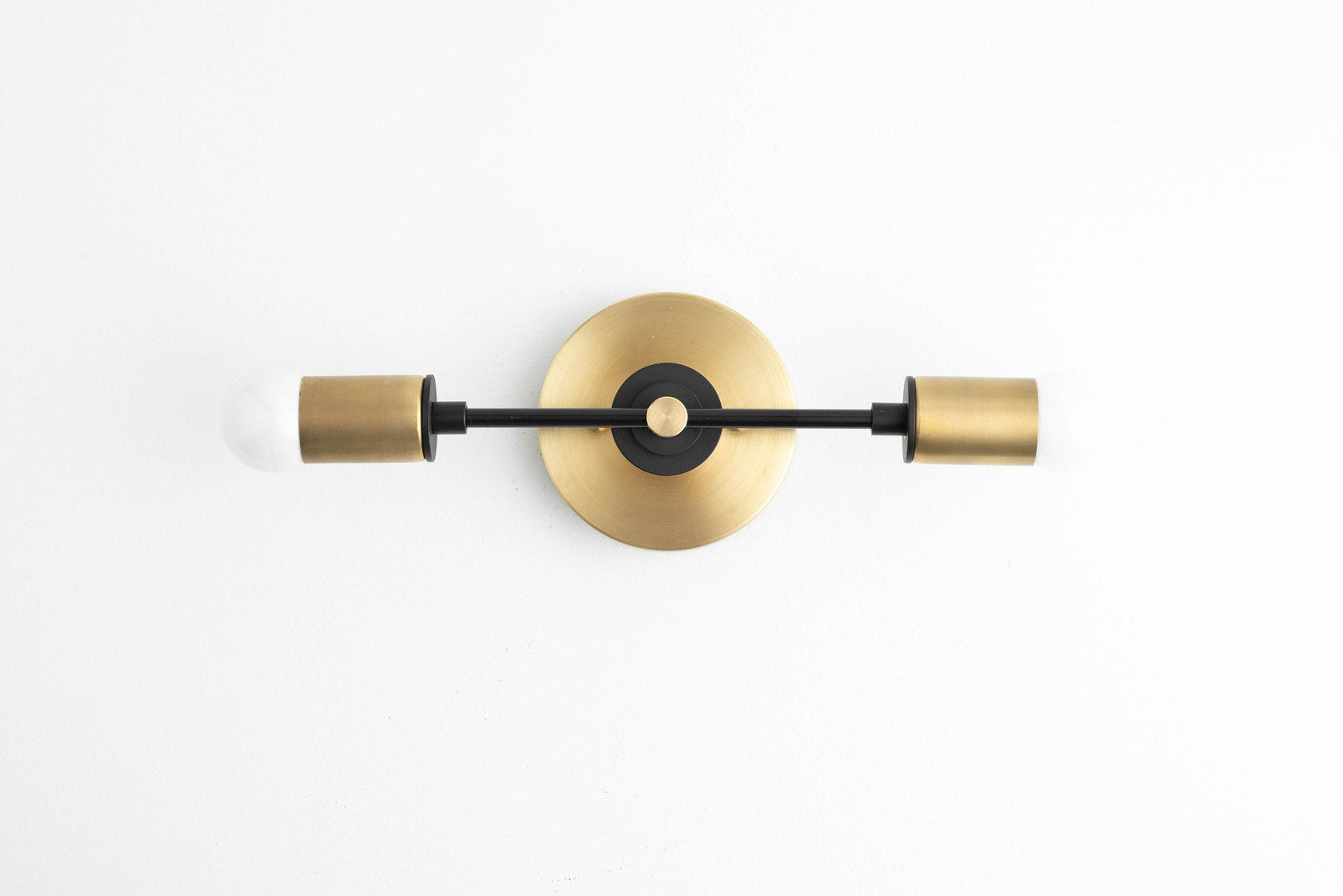 Art Deco vanity light with black metal arms and raw brass cylindrical shades mounted on a round brass backplate. - VANITY LIGHT MODEL NO. 8057