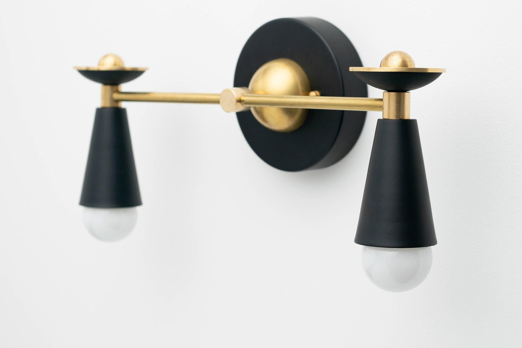 Two-bulb Art Deco vanity light with black cone shades and raw brass accents mounted on black round base. - VANITY LIGHT MODEL NO. 4517
