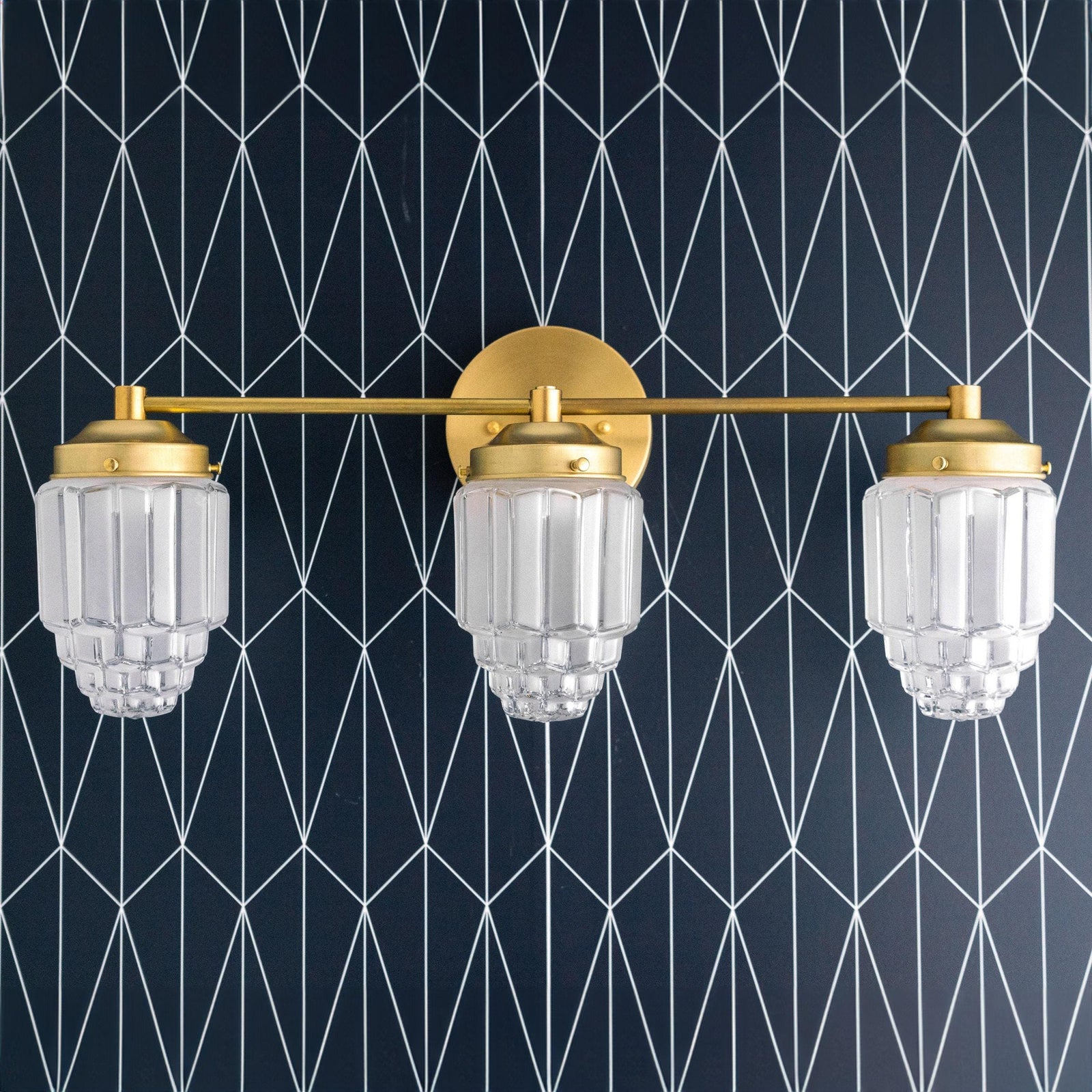 Art Deco vanity light with three clear globe shades and raw brass finish against geometric black wall. - VANITY LIGHT MODEL NO. 3918