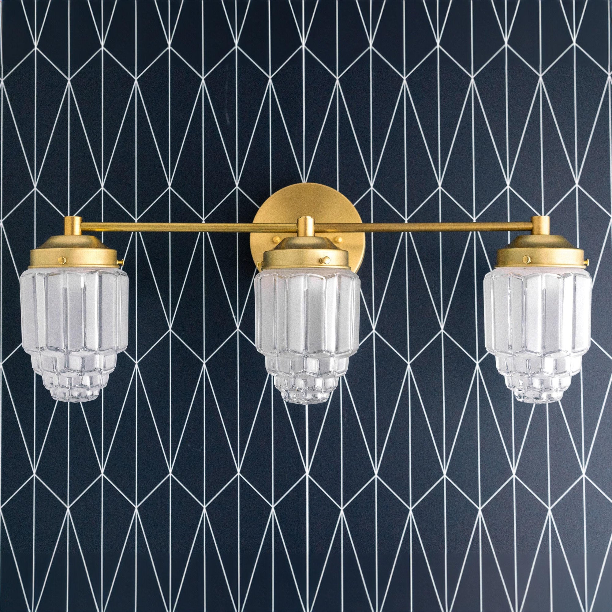 Art Deco vanity light with three clear globe shades and raw brass finish against geometric black wall. - VANITY LIGHT MODEL NO. 3918