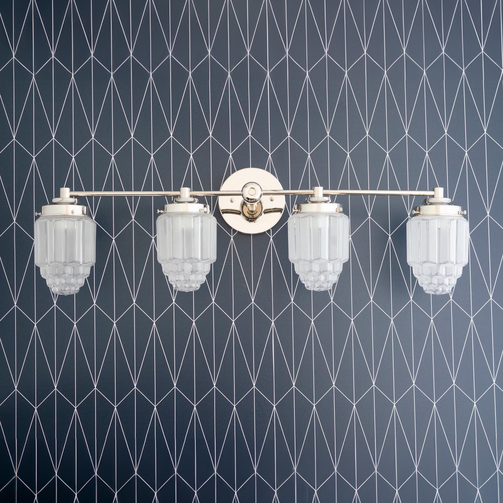 Polished nickel 4-bulb art deco vanity light with frosted globe shades and geometric wall pattern background. - VANITY LIGHT MODEL NO. 1082