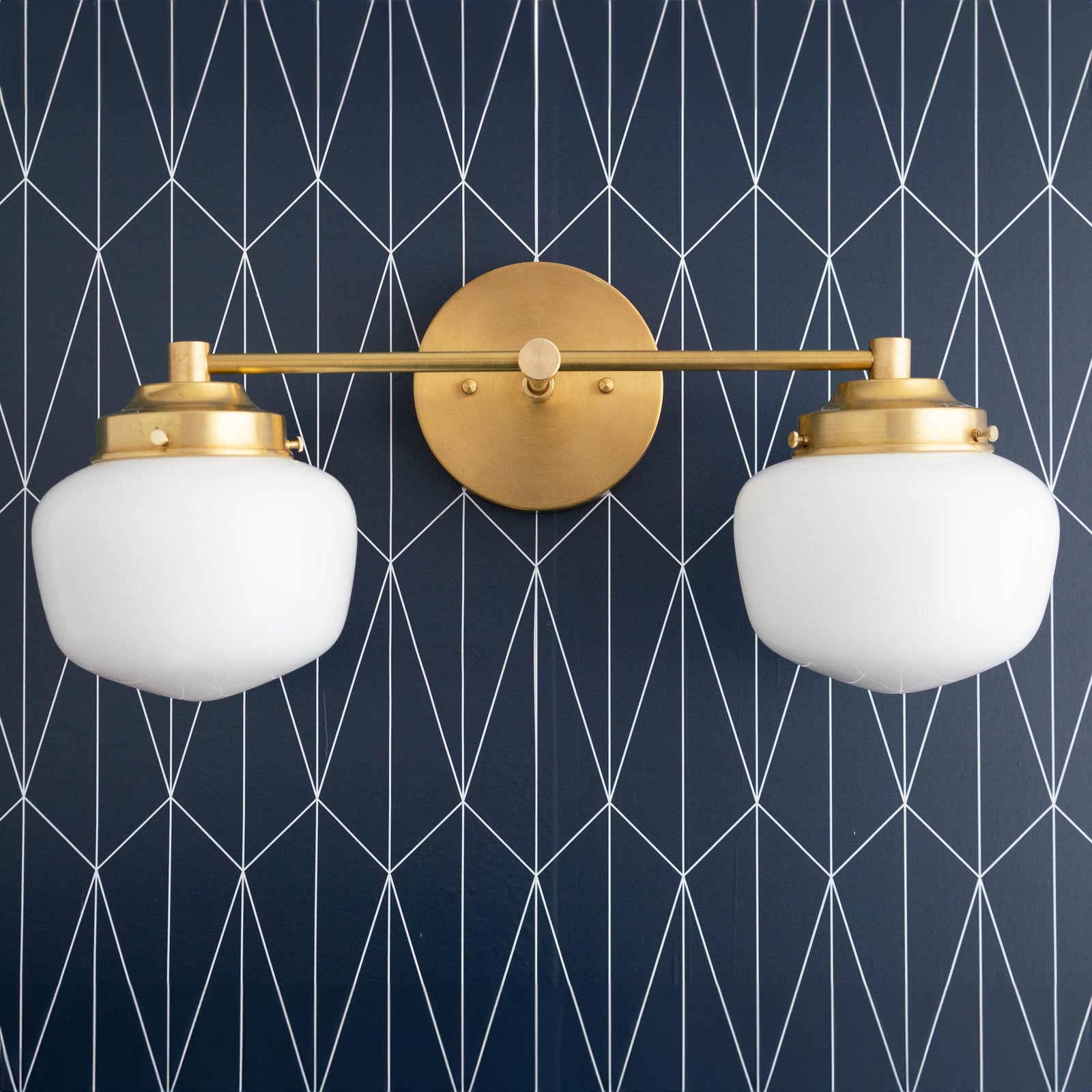 Art Deco two-bulb vanity light in polished brass with white glass globe shades against dark geometric wallpaper. - VANITY LIGHT MODEL NO. 5799