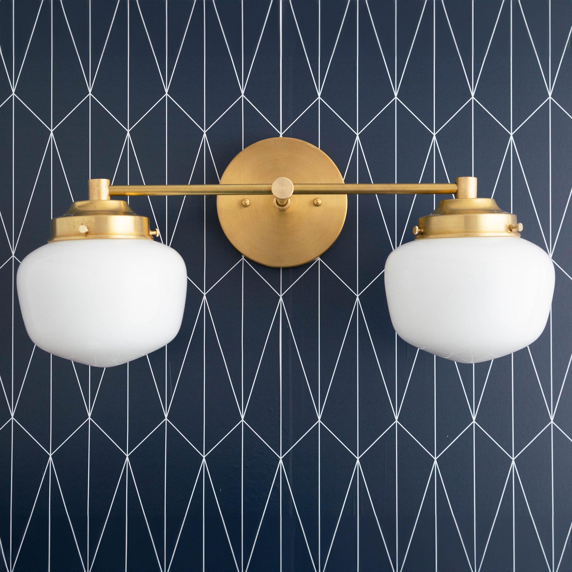 Art Deco two-bulb vanity light in polished brass with white glass globe shades against dark geometric wallpaper. - VANITY LIGHT MODEL NO. 5799