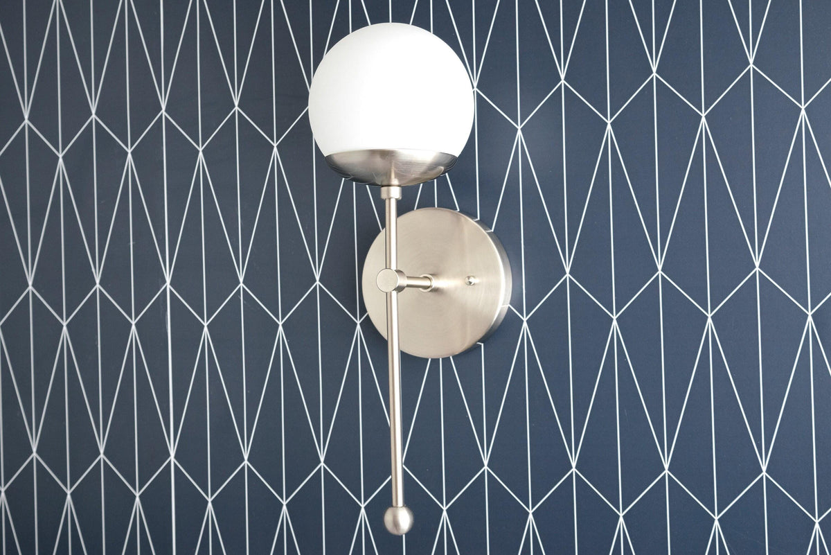 Art Deco brushed nickel sconce with white globe shade and sleek vertical rod mount on geometric navy wall. - SCONCE MODEL NO. 1048