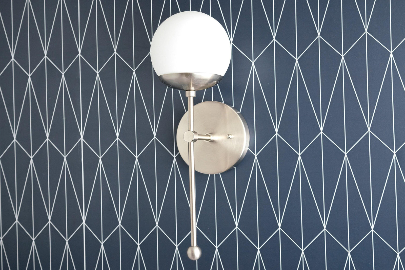 Art Deco brushed nickel sconce with white globe shade and sleek vertical rod mount on geometric navy wall. - SCONCE MODEL NO. 1048