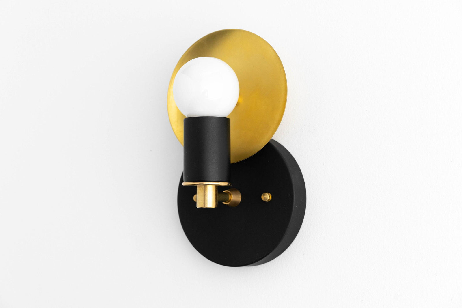 Black matte wall sconce with round brass backplate and exposed white globe bulb. - SCONCE MODEL NO. 8677