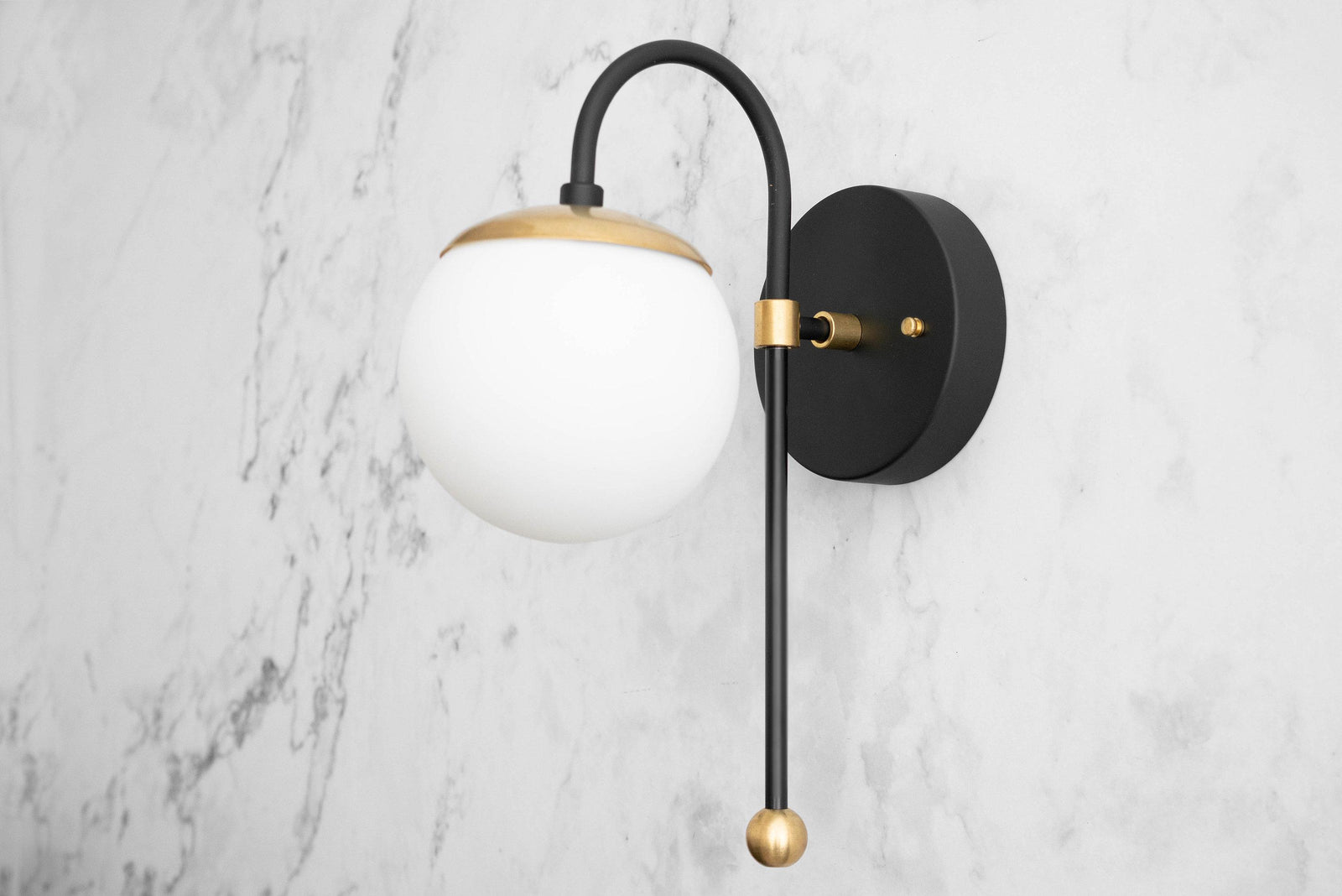 Black metal wall sconce with white globe shade and brass accent details on marble background. - SCONCE MODEL NO. 1045