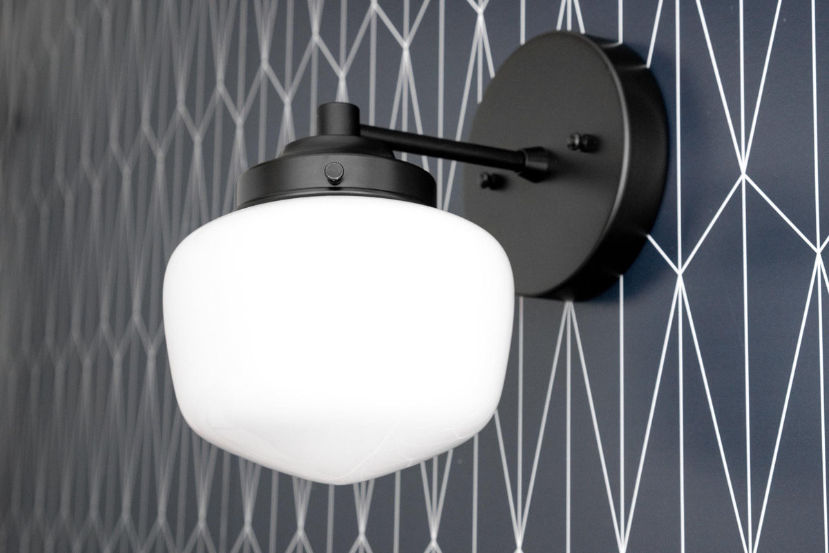Black metal Art Deco wall sconce with white globe shade mounted on textured gray wall. - SCONCE MODEL NO. 7321
