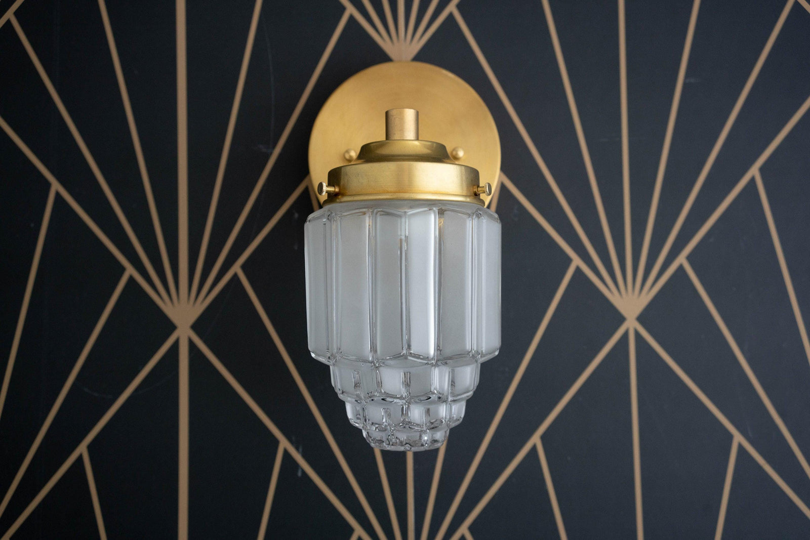 Art Deco brass wall sconce with tiered frosted globe shade against black geometric wallpaper. - SCONCE MODEL NO. 6130