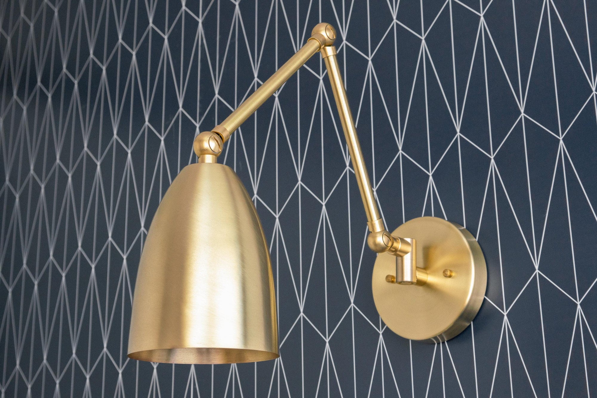 Adjustable raw brass wall sconce with slender arm and dome-shaped shade against geometric wallpaper. - SCONCE MODEL NO. 0107