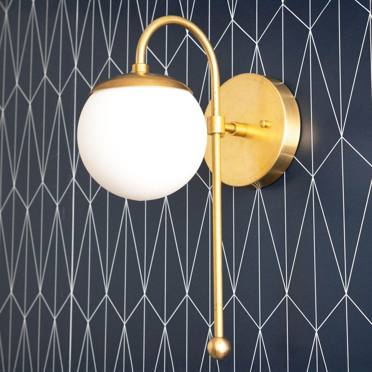 Art Deco style wall sconce with raw brass finish and white globe shade against dark geometric background. - SCONCE MODEL NO. 1045