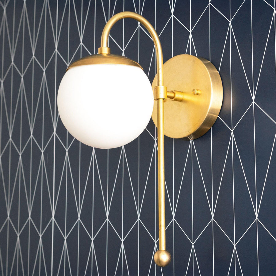 Art Deco style wall sconce with raw brass finish and white globe shade against dark geometric background. - SCONCE MODEL NO. 1045