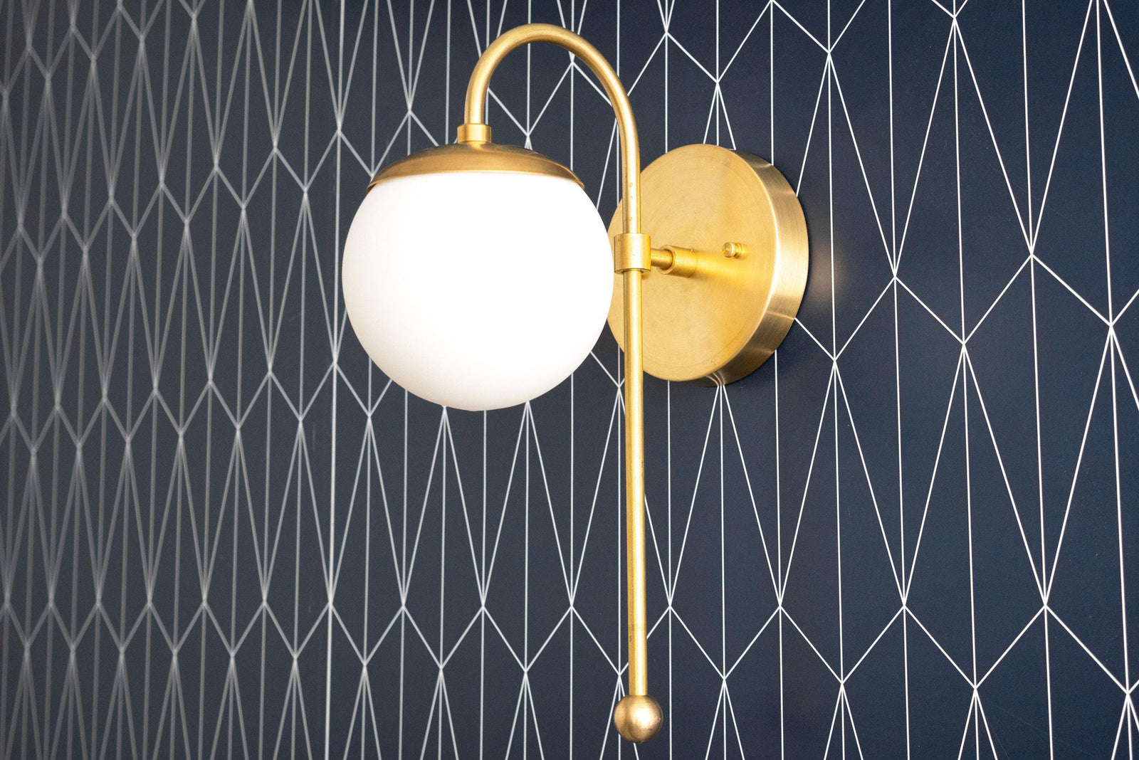 Art Deco raw brass wall sconce with round white globe and curved arm on geometric black wallpaper background. - SCONCE MODEL NO. 1045