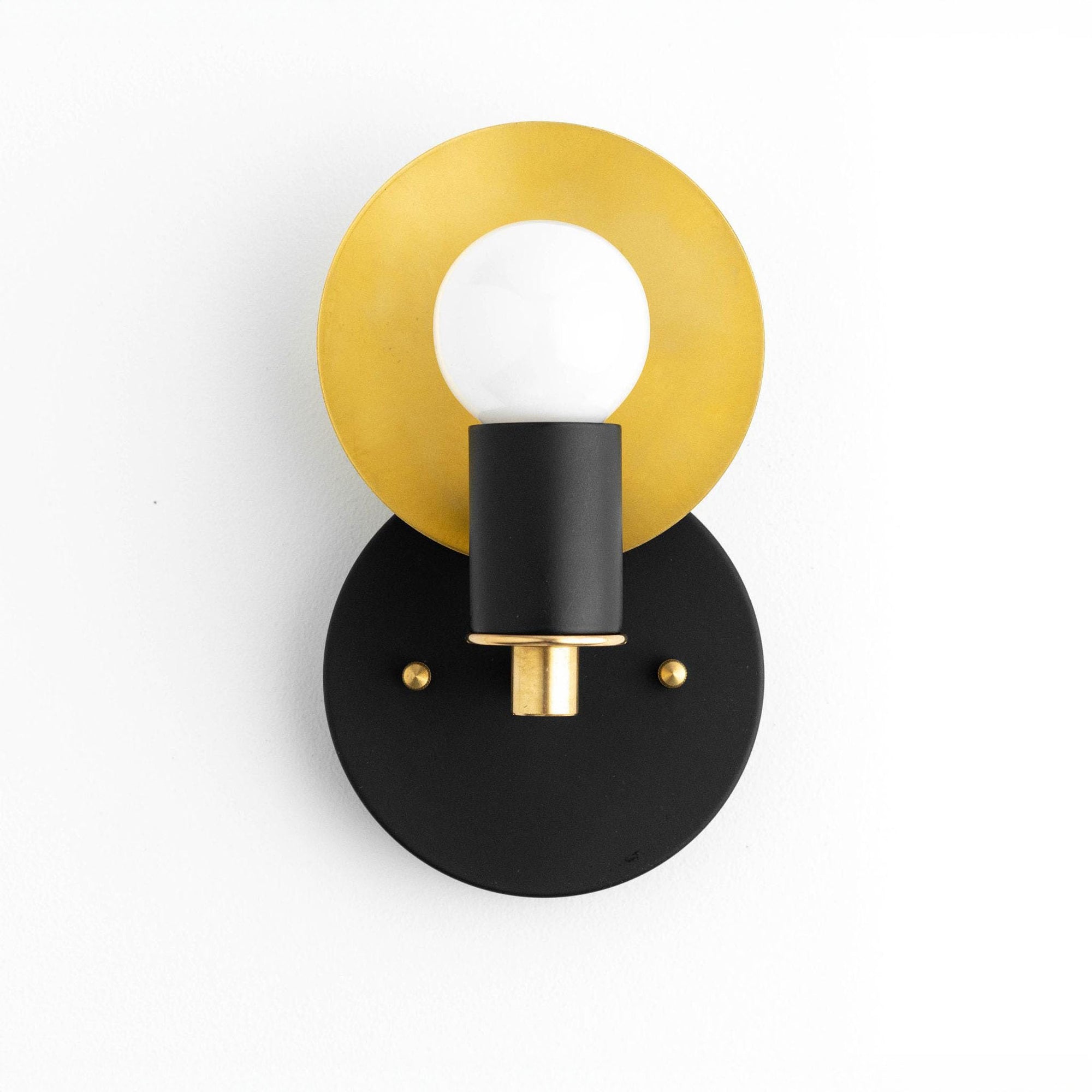 Art Deco wall sconce with black circular base, brass disc backplate, and bare bulb fixture. - SCONCE MODEL NO. 8677