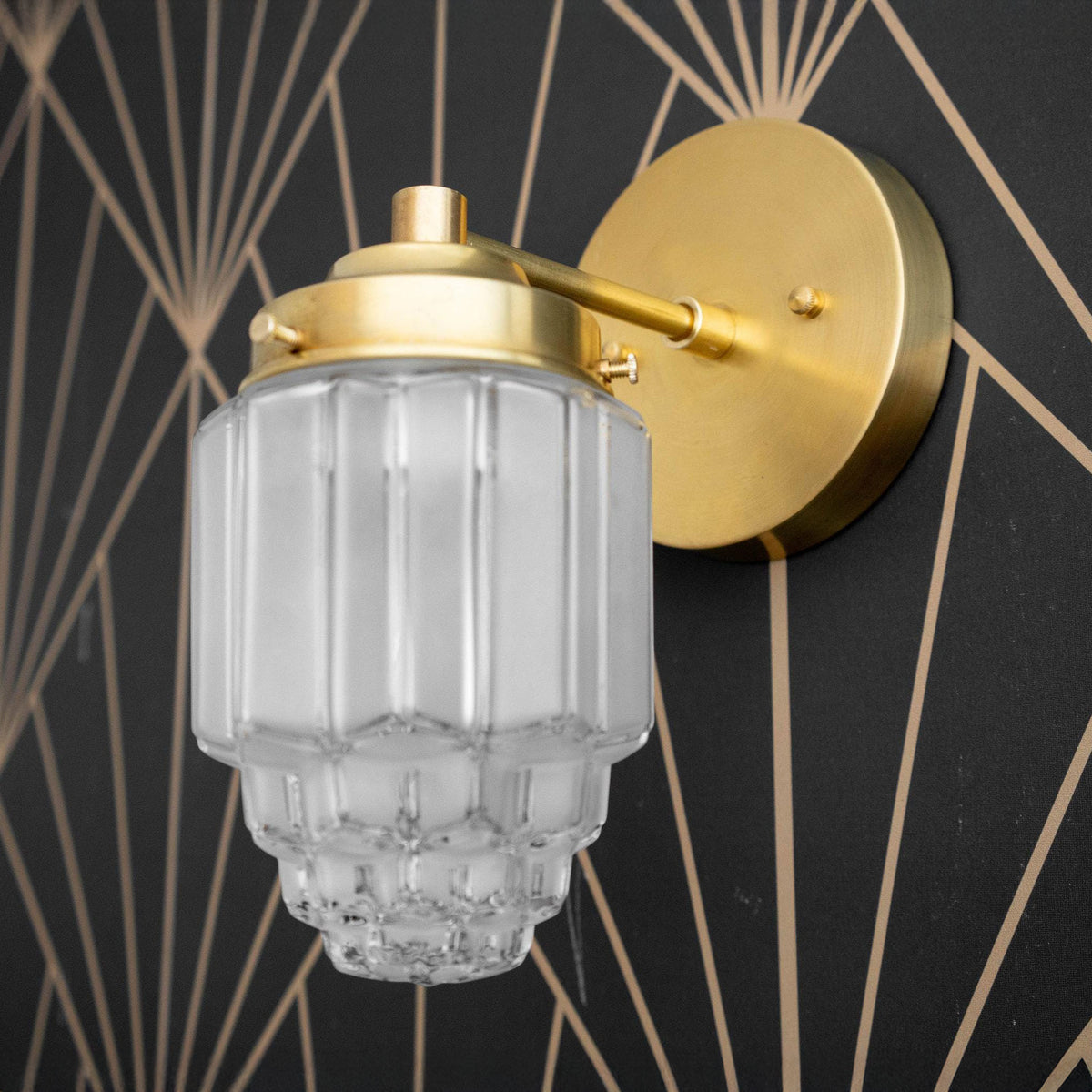 Art Deco sconce with frosted globe shade and raw brass finish on geometric black wall. - SCONCE MODEL NO. 6130