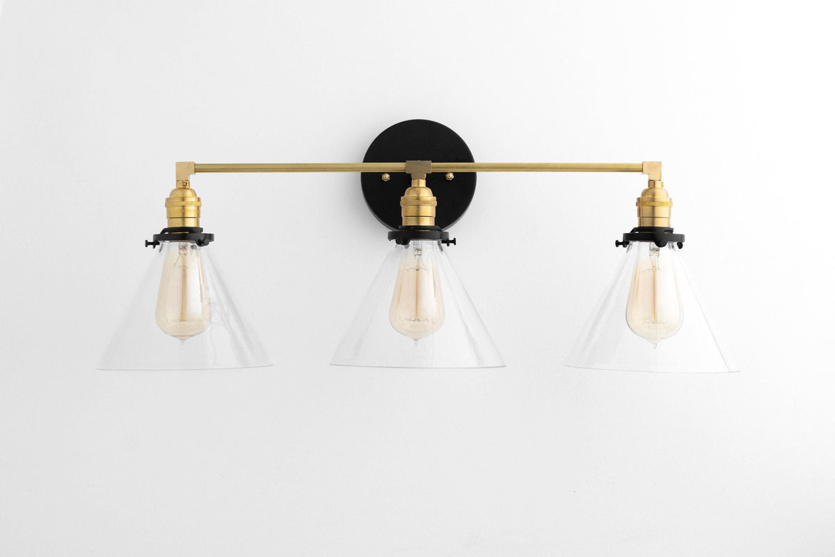 Mid-century modern vanity light with three clear cone shades and raw brass finish mounted on a black circular base. - VANITY LIGHT MODEL NO. 5219
