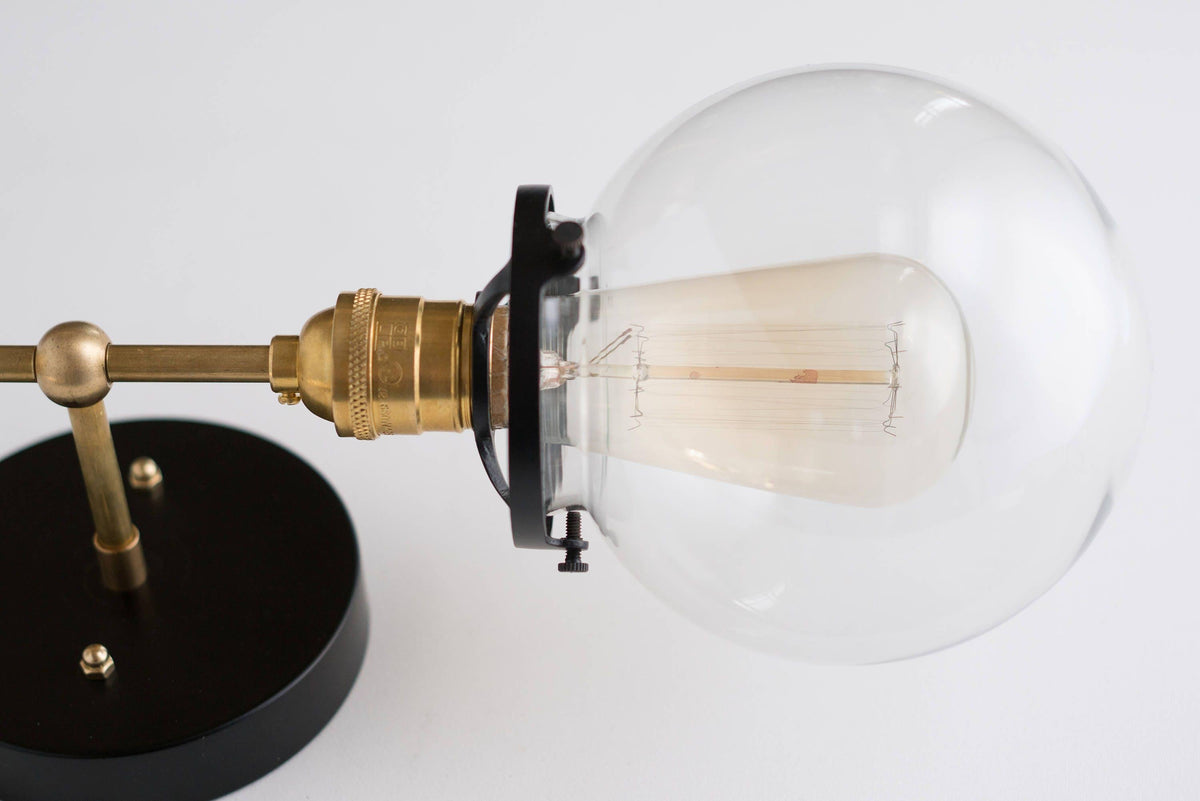Mid-century modern vanity light with clear globe bulb, raw brass arm, and black round base. - VANITY LIGHT MODEL NO. 7350