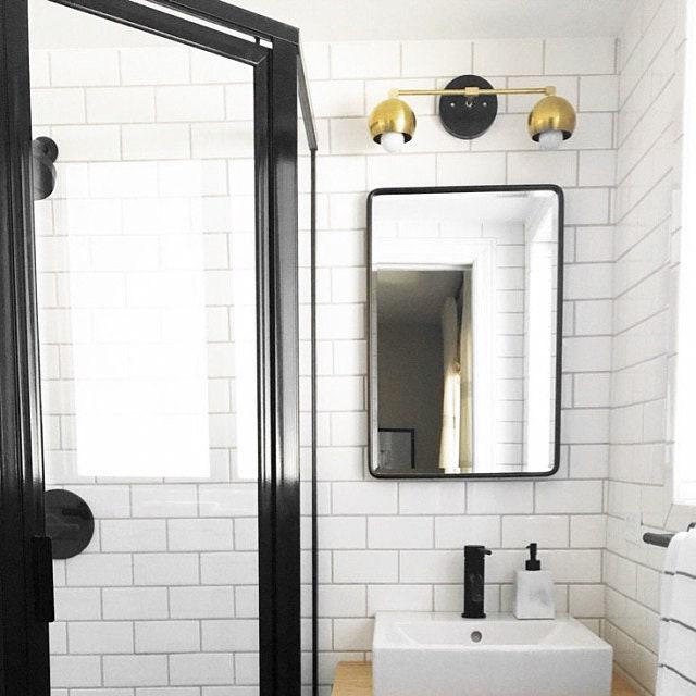 Mid-century modern 2-bulb vanity light with sealed brass finish and exposed bulbs above black-framed rectangular mirror. - VANITY LIGHT MODEL NO. 5469