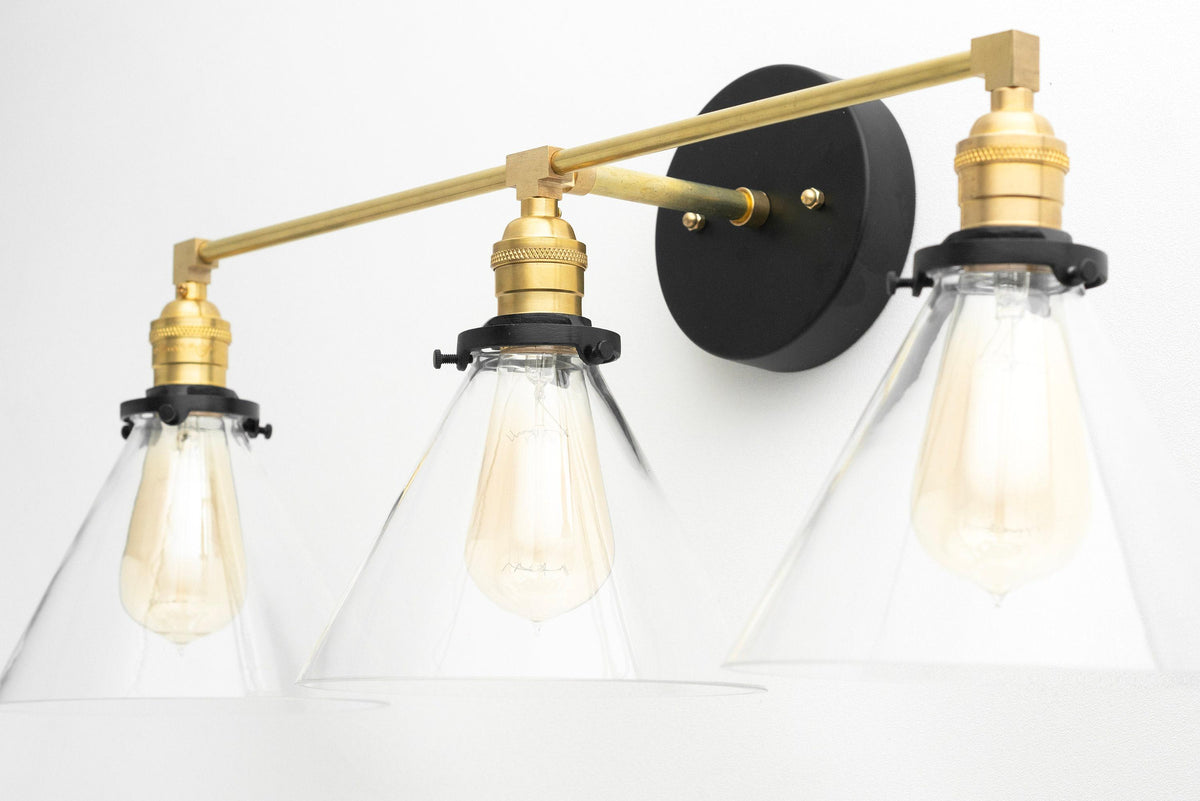 Mid-century modern vanity light with three clear conical glass shades and raw brass finish mounting on a black circular base. - VANITY LIGHT MODEL NO. 5219