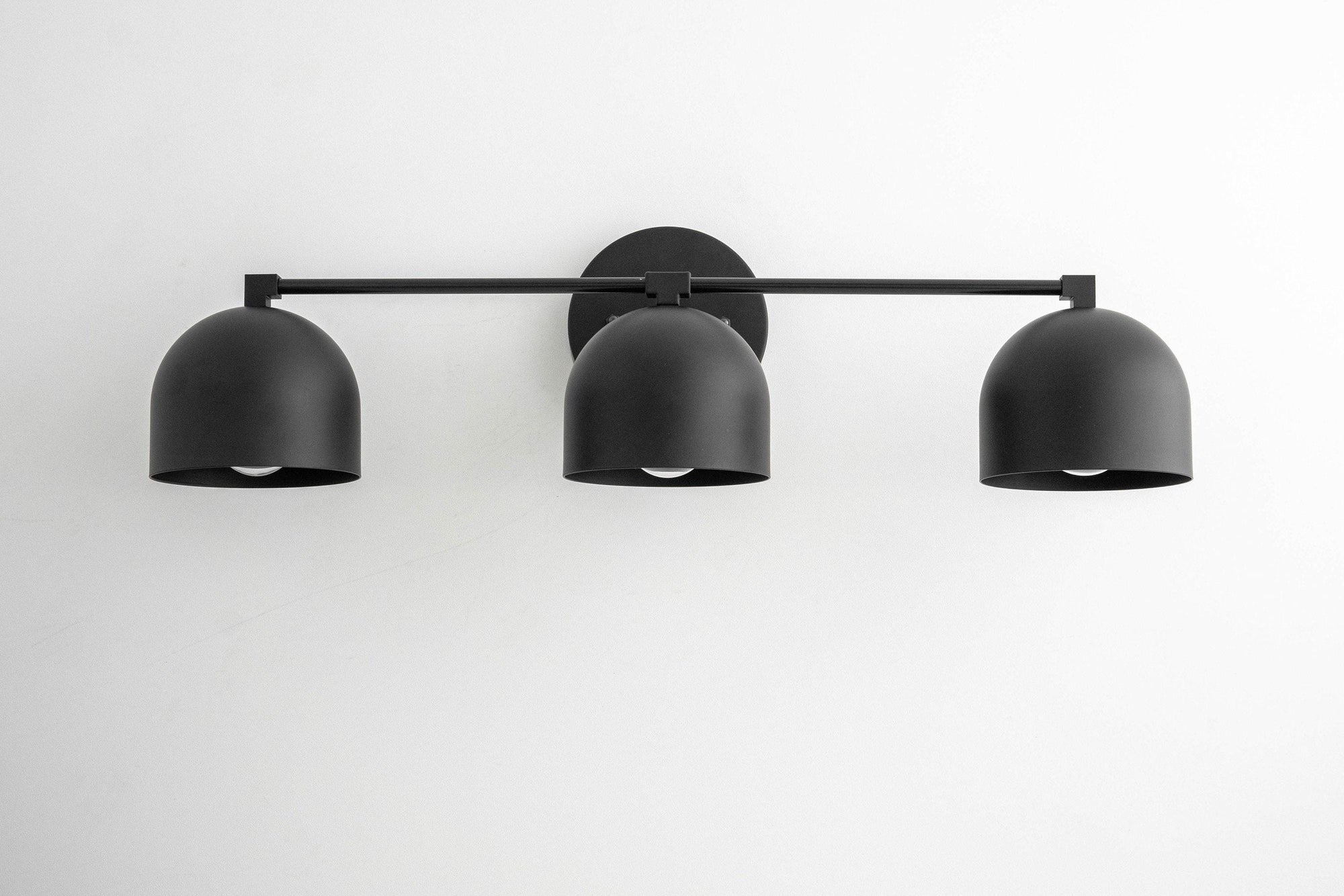 Mid-century modern black metal vanity light with three dome-shaped shades mounted on a horizontal bar. - VANITY LIGHT MODEL NO. 7565