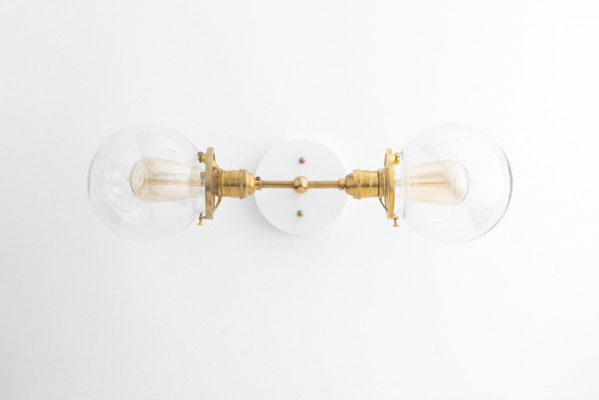 Two-bulb vanity light with raw brass finish and clear globe bulbs mounted on a round white wall plate. - VANITY LIGHT MODEL NO. 7350