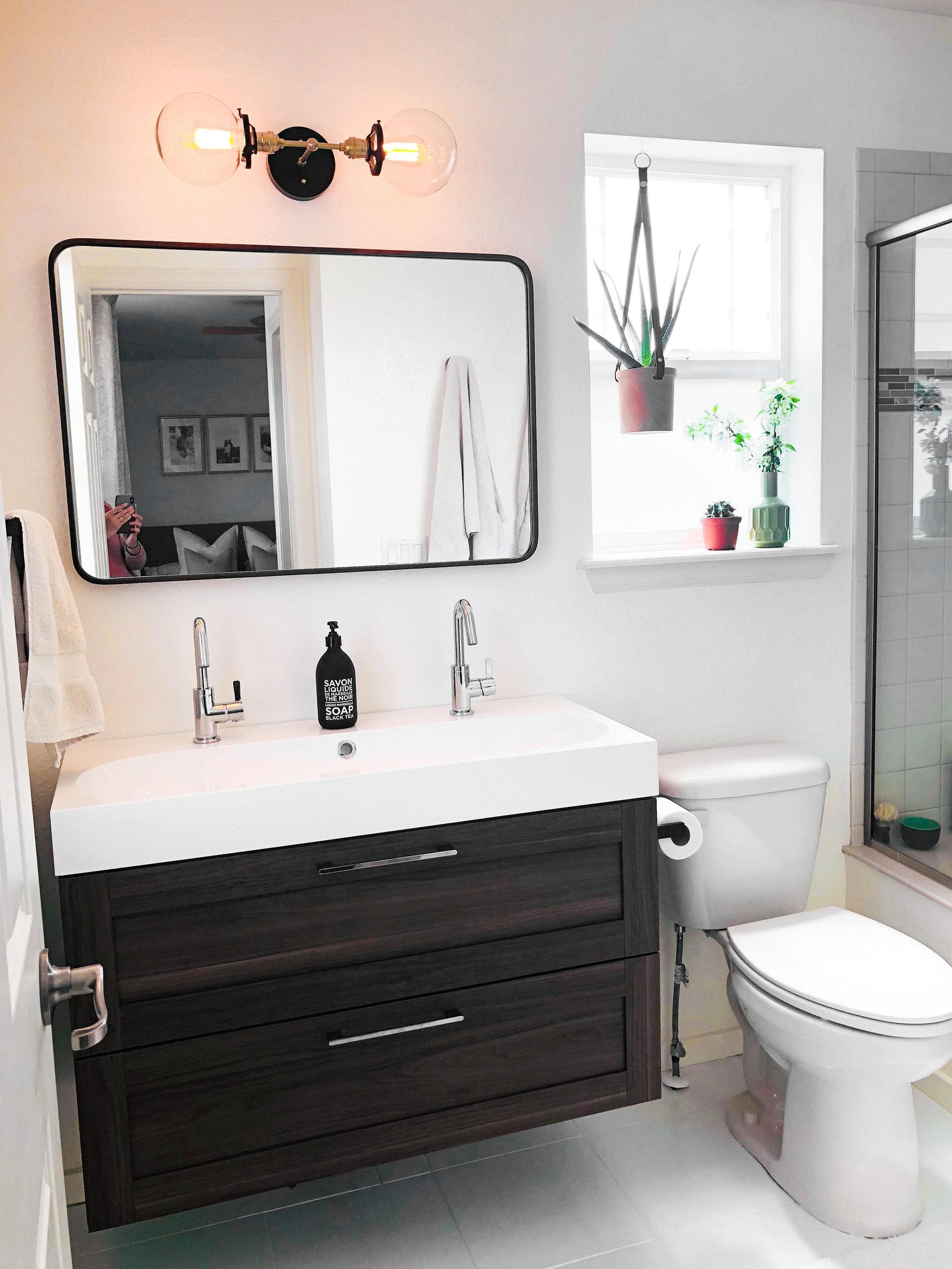 Black metal vanity light with two clear globe bulbs mounted above a rectangular mirror in a modern bathroom. - VANITY LIGHT MODEL NO. 7350