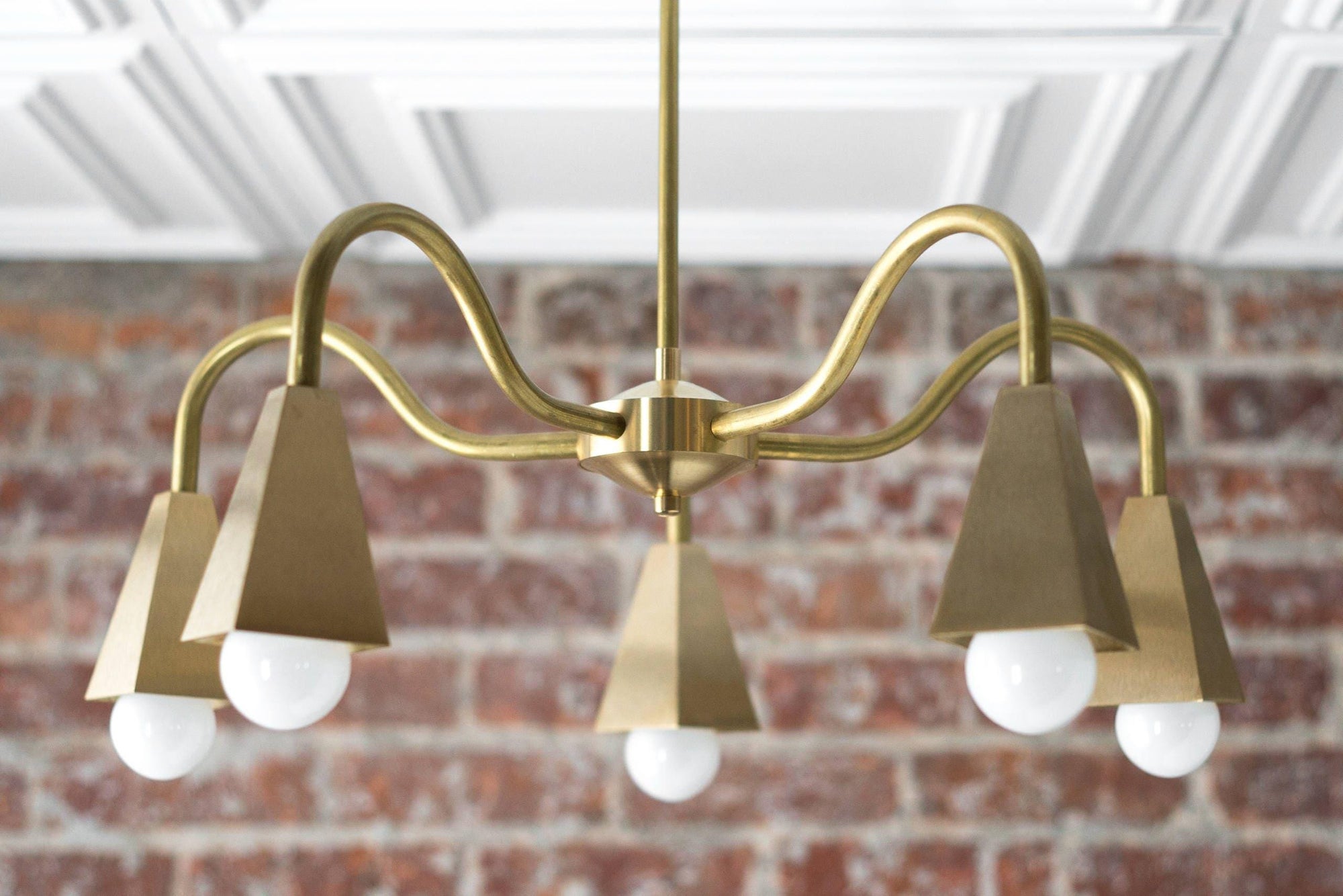 Mid-century modern raw brass chandelier with four conical shades and exposed bulbs against a brick wall background. - CHANDELIER MODEL NO. 2464
