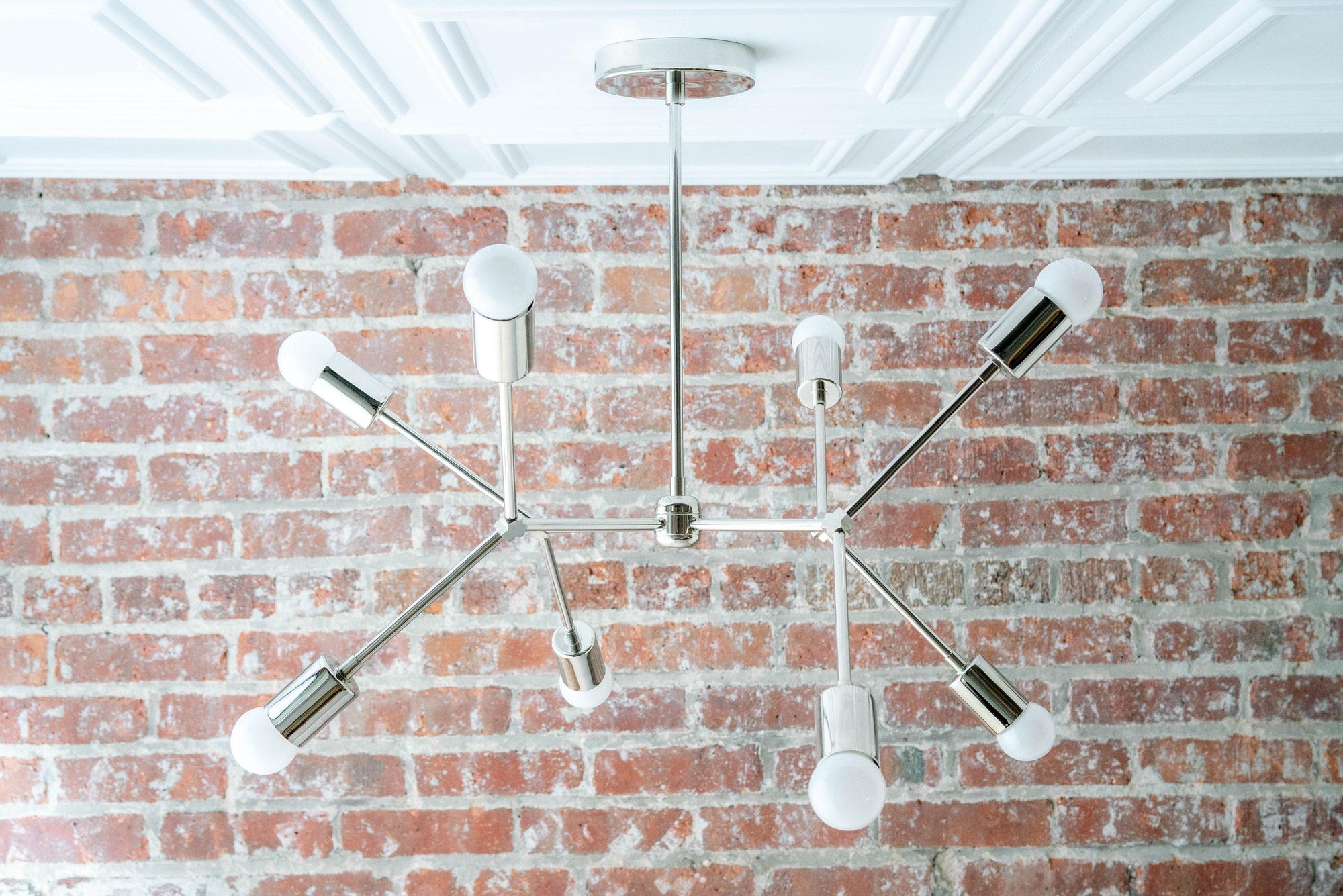 Mid-century modern raw brass chandelier with six exposed bulbs and sleek arms against a brick wall. - CHANDELIER MODEL NO. 5056