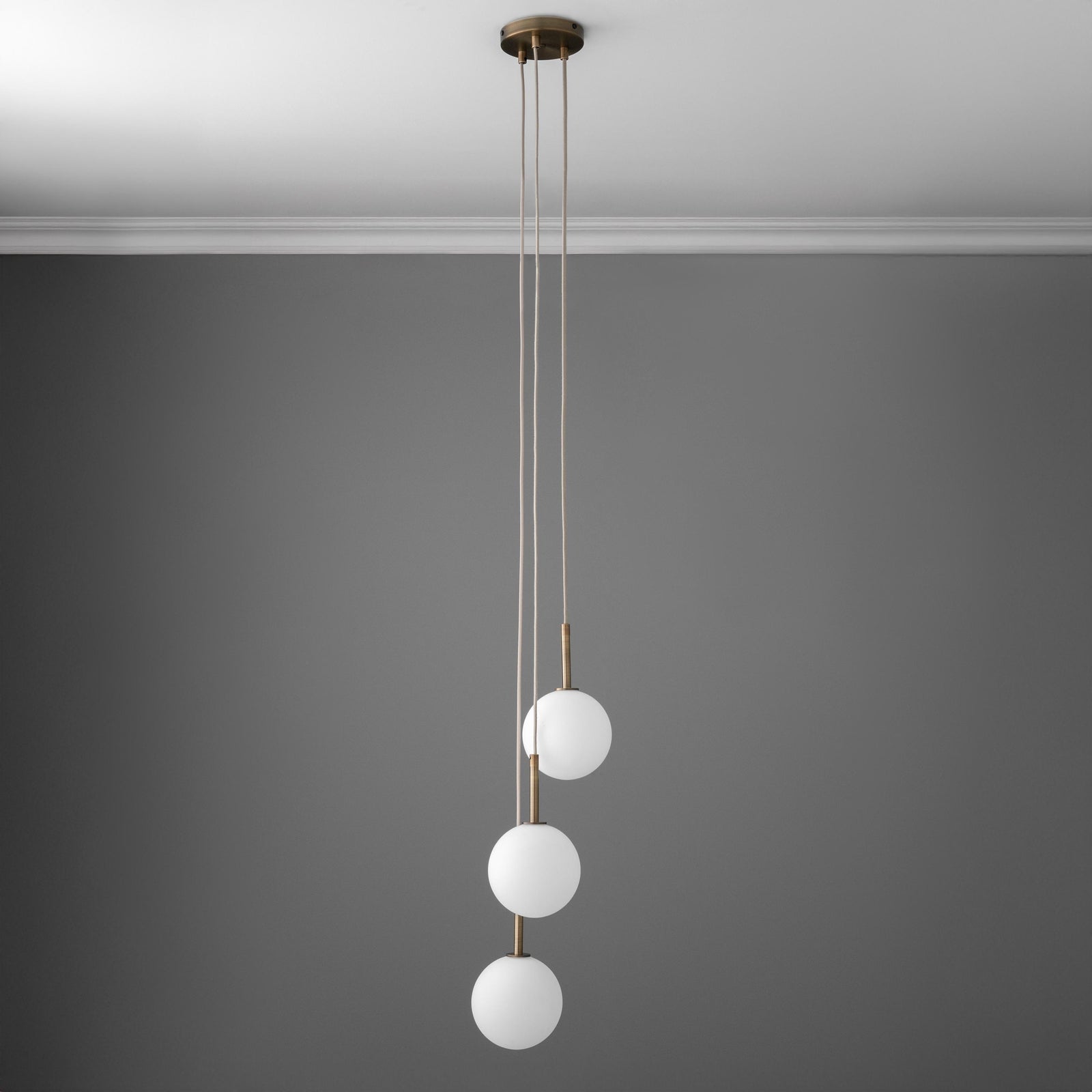 Minimalist chandelier with three white globe lights hanging vertically on antique brass rods against a gray wall. - CHANDELIER MODEL NO. 4701