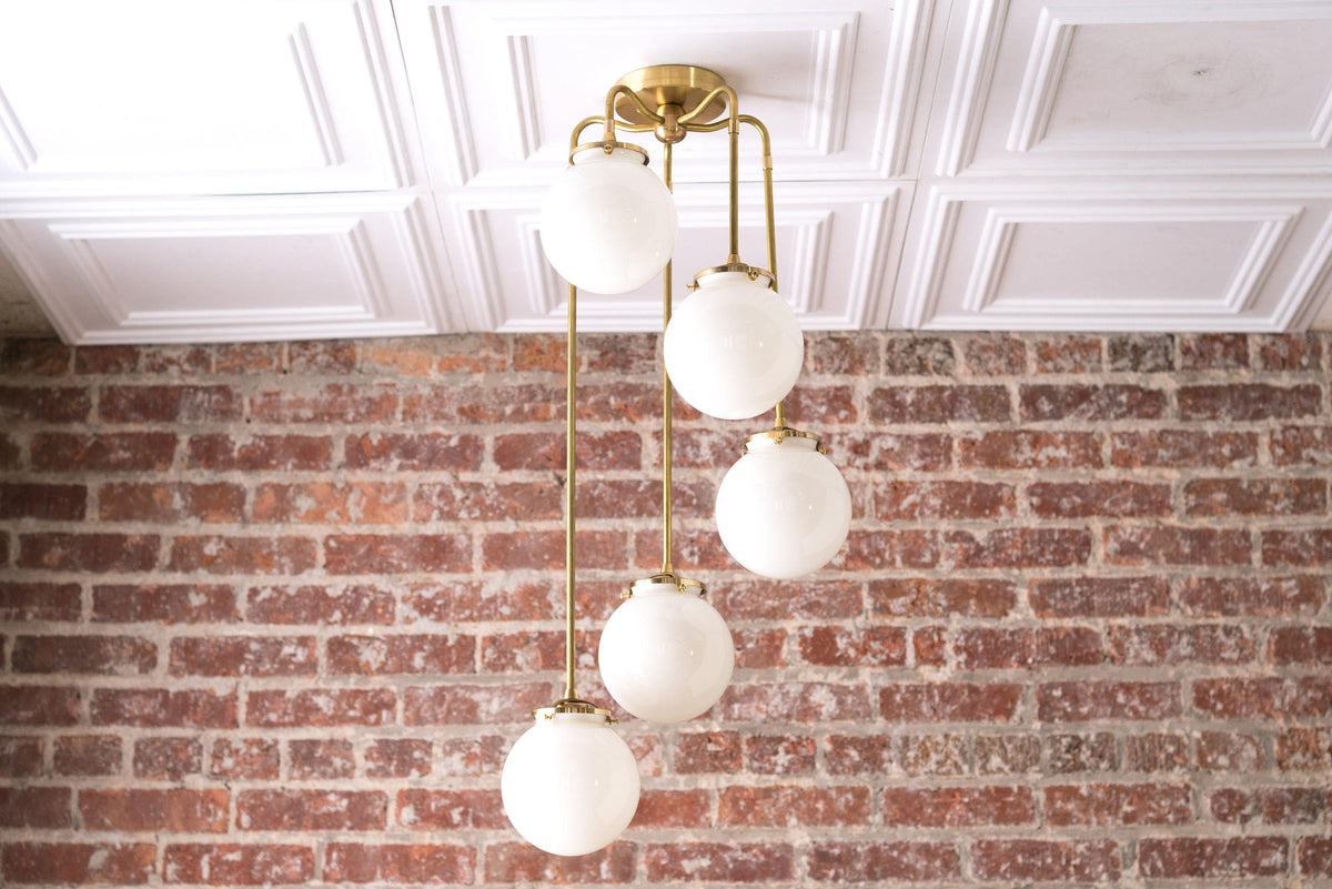 Mid-century modern raw brass chandelier with six white globe lights hanging in staggered arrangement. - CHANDELIER MODEL NO. 1809