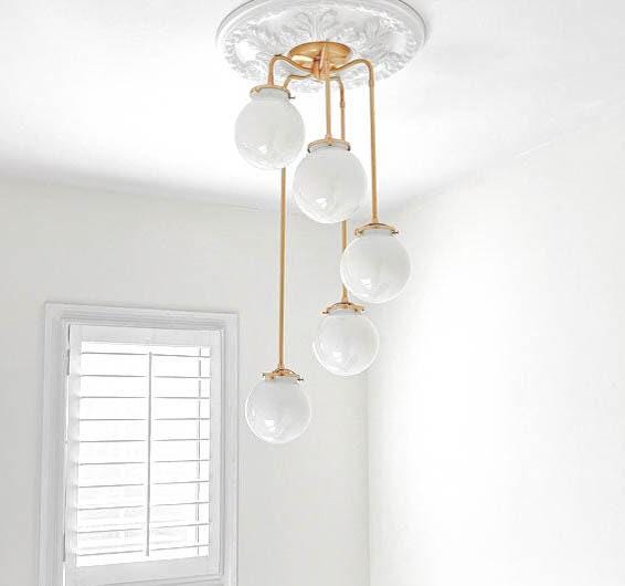 Mid-century modern chandelier with five white glass globes on raw brass rods hanging from decorative ceiling mount. - CHANDELIER MODEL NO. 1809