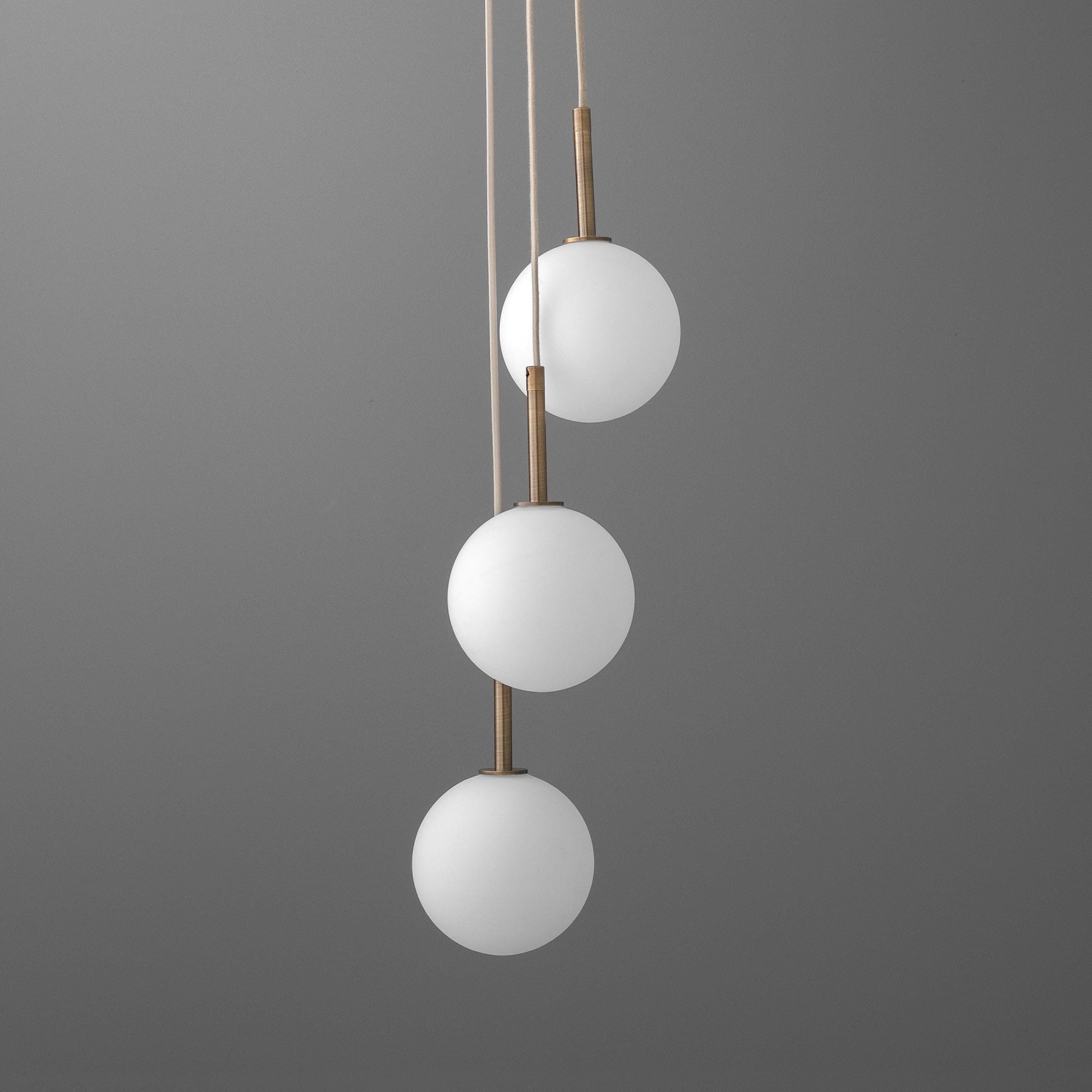 Three-tier chandelier with frosted white glass globes and brushed brass accents hanging on tan cords against gray background. - CHANDELIER MODEL NO. 4701