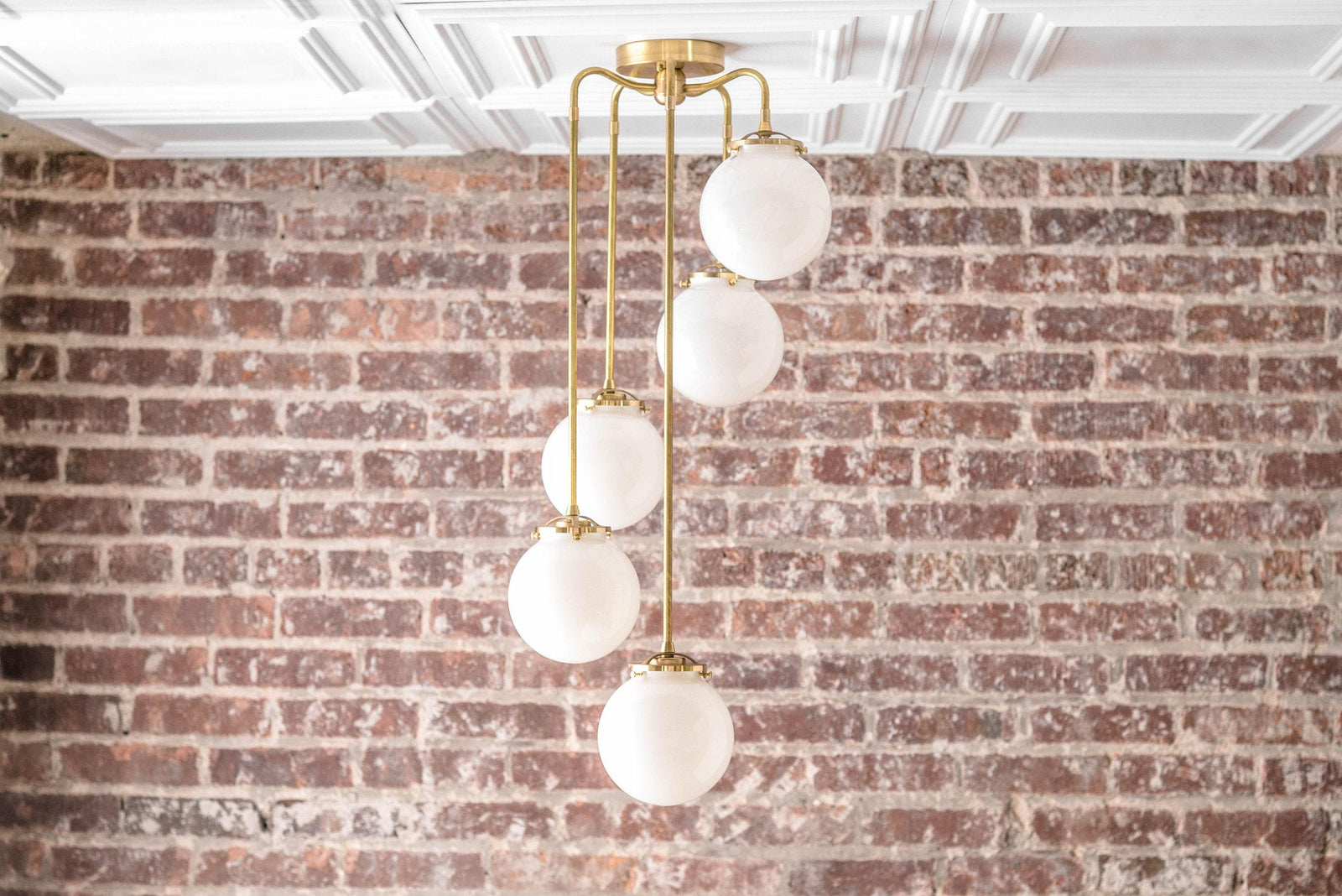 Mid-century modern chandelier with five white globe lights on raw brass rods against a brick wall background. - CHANDELIER MODEL NO. 1809