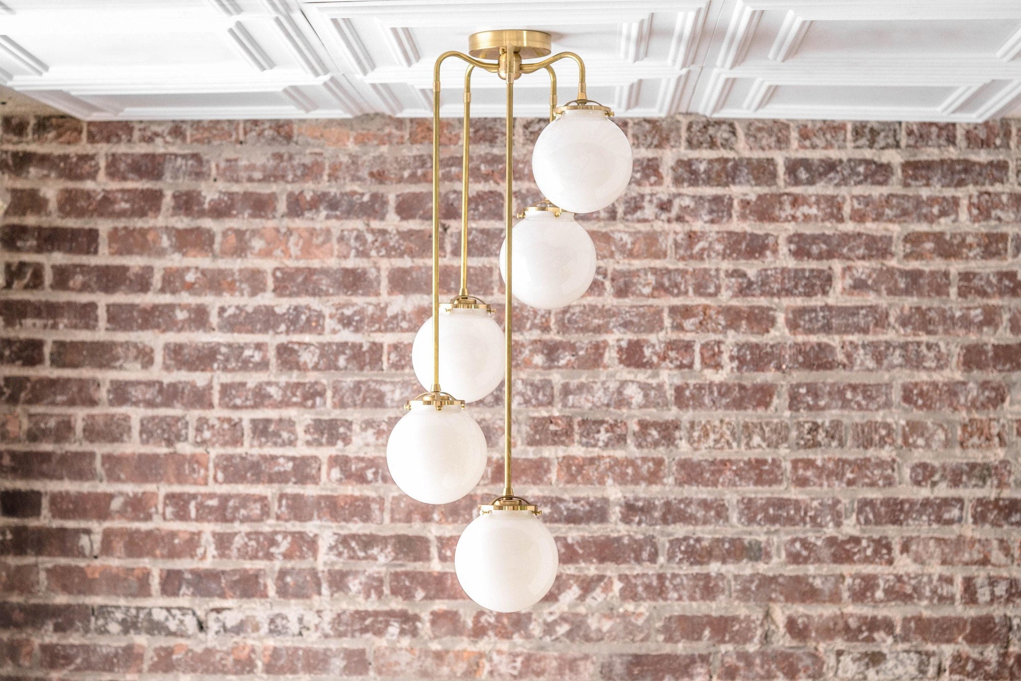 Mid-century modern chandelier with five white globe lights on raw brass rods against a brick wall background. - CHANDELIER MODEL NO. 1809