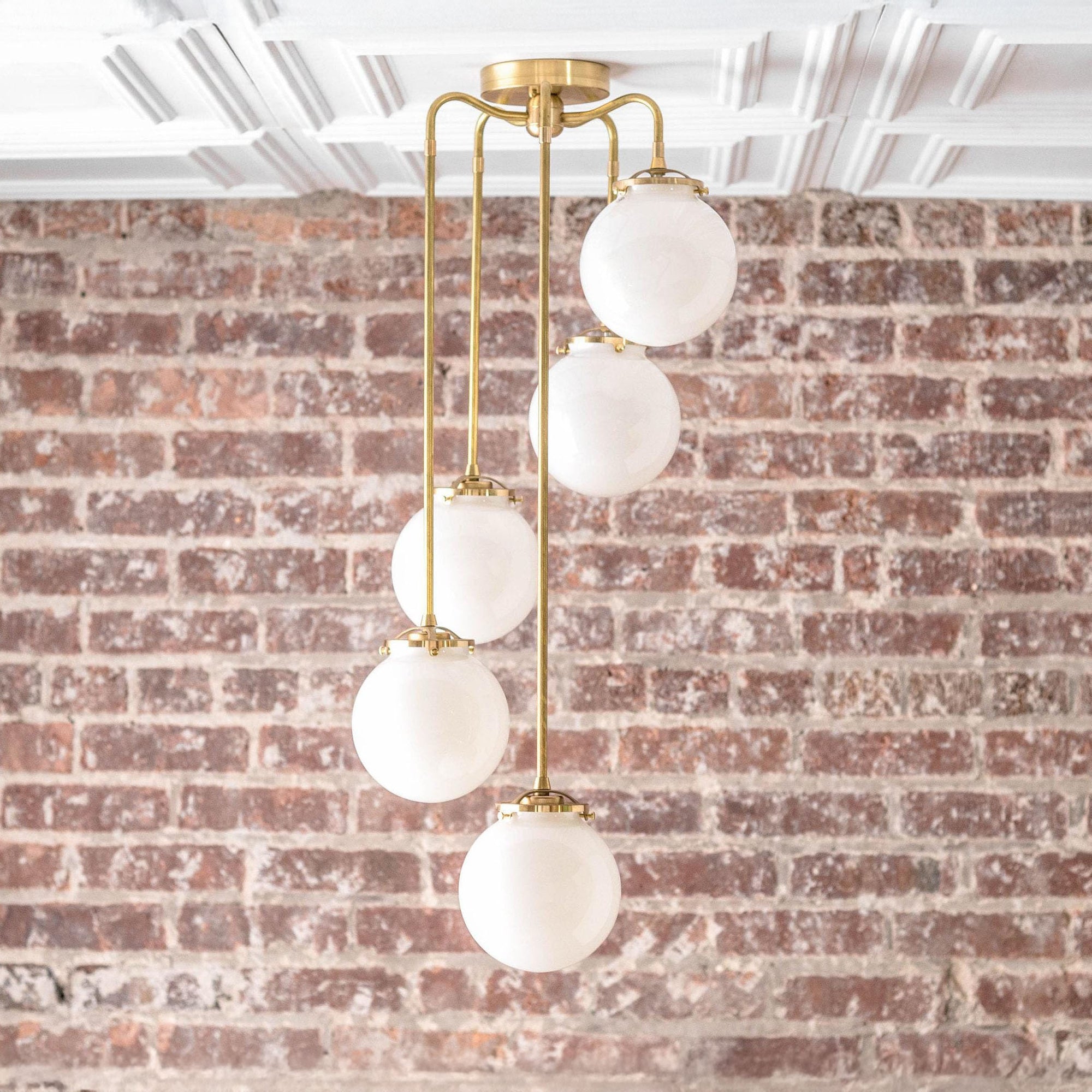 Mid-century modern chandelier with five white glass globes and raw brass rods against an exposed brick wall. - CHANDELIER MODEL NO. 1809