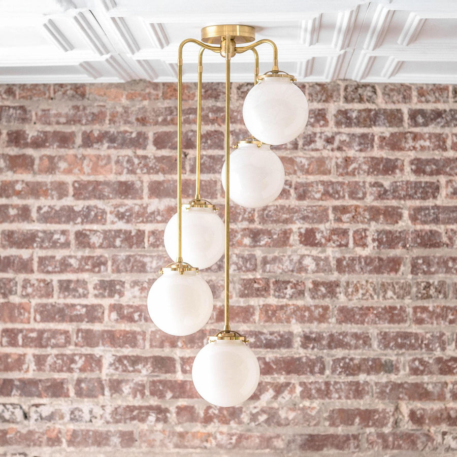 Mid-century modern chandelier with five white glass globes and raw brass rods against an exposed brick wall. - CHANDELIER MODEL NO. 1809