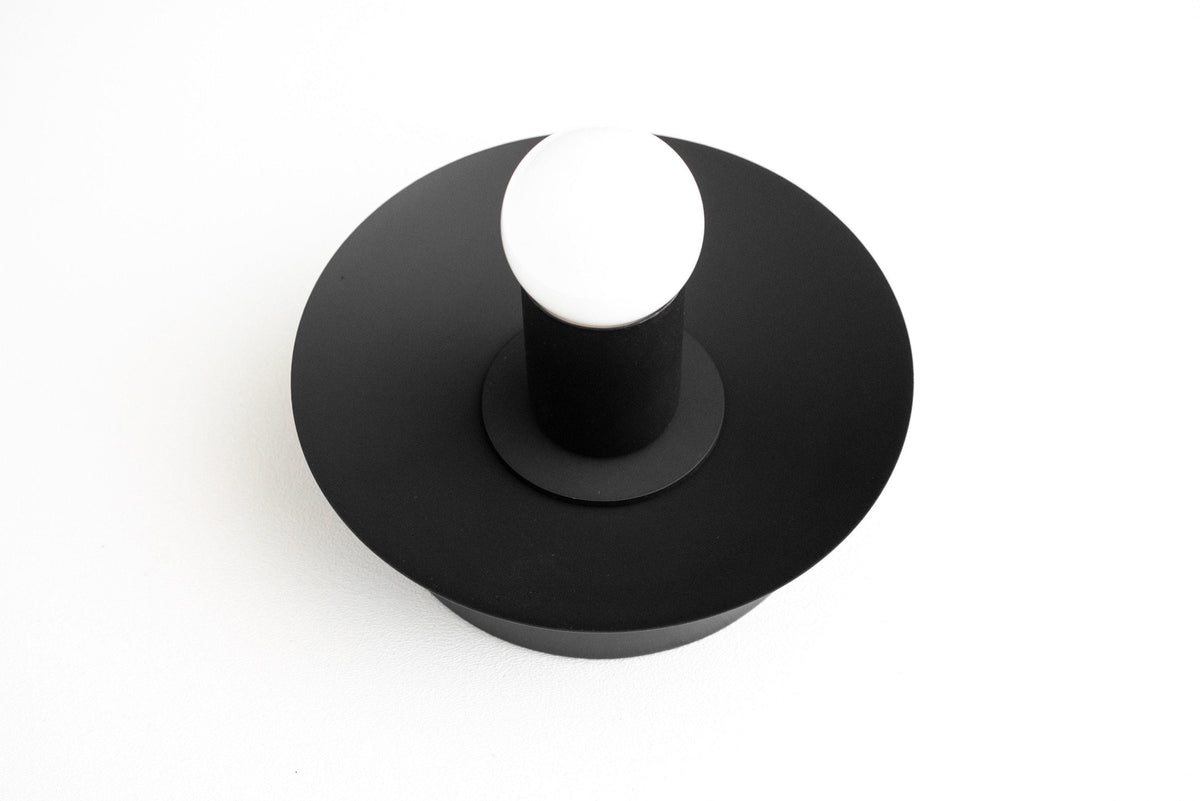 Matte black metal wall sconce with wide round base and exposed bulb design. - SCONCE MODEL NO. 7004