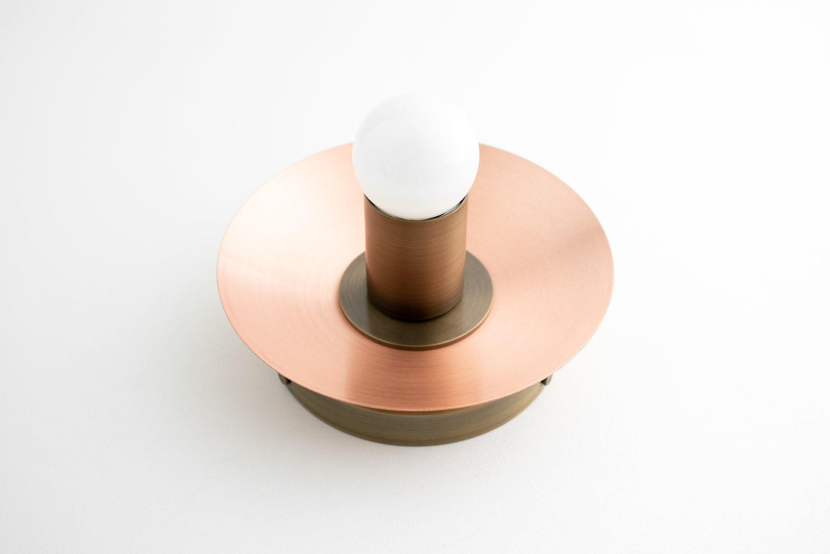 Flush mount sconce with round copper disc and exposed white bulb on antique brass base. - SCONCE MODEL NO. 7004
