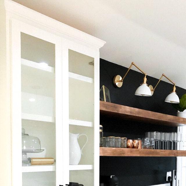 Mid-century modern adjustable wall sconce with white shades and raw brass finish above wooden shelves. - SCONCE MODEL NO. 8551