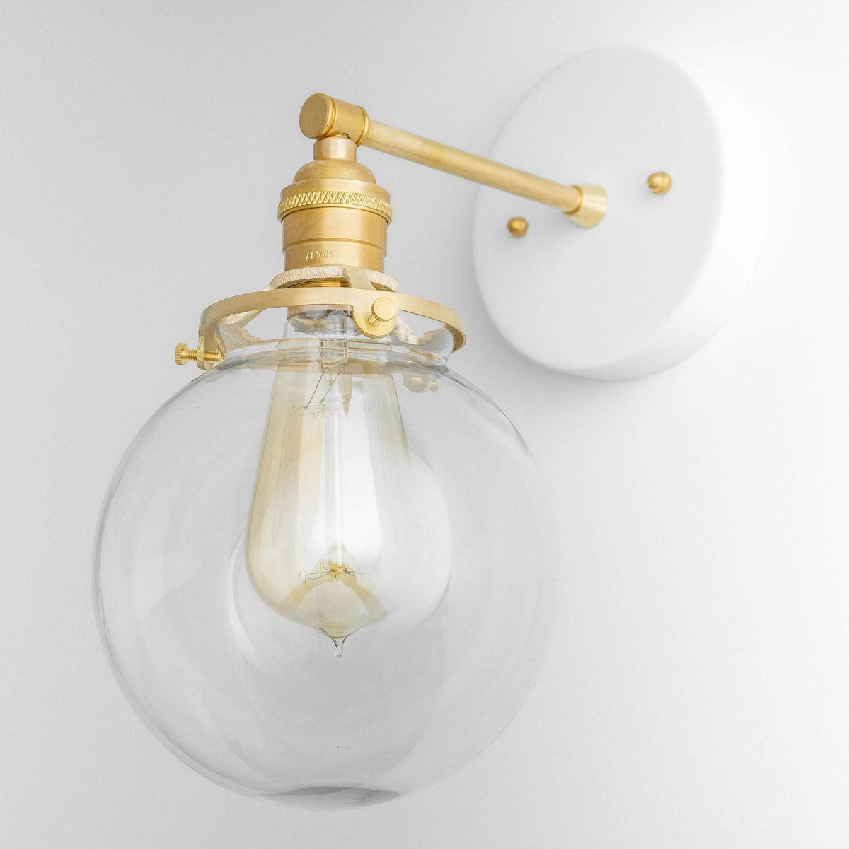 Mid-century modern globe sconce with clear glass shade and raw brass finish mounted on white circular backplate. - SCONCE MODEL NO. 5456