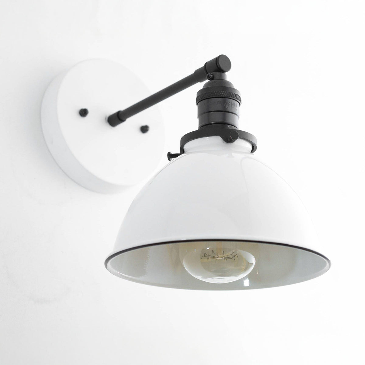Sconce with a White round backplate and metal dome shade and a Black arm and socket over an exposed filament bulb. - SCONCE MODEL NO. 7026