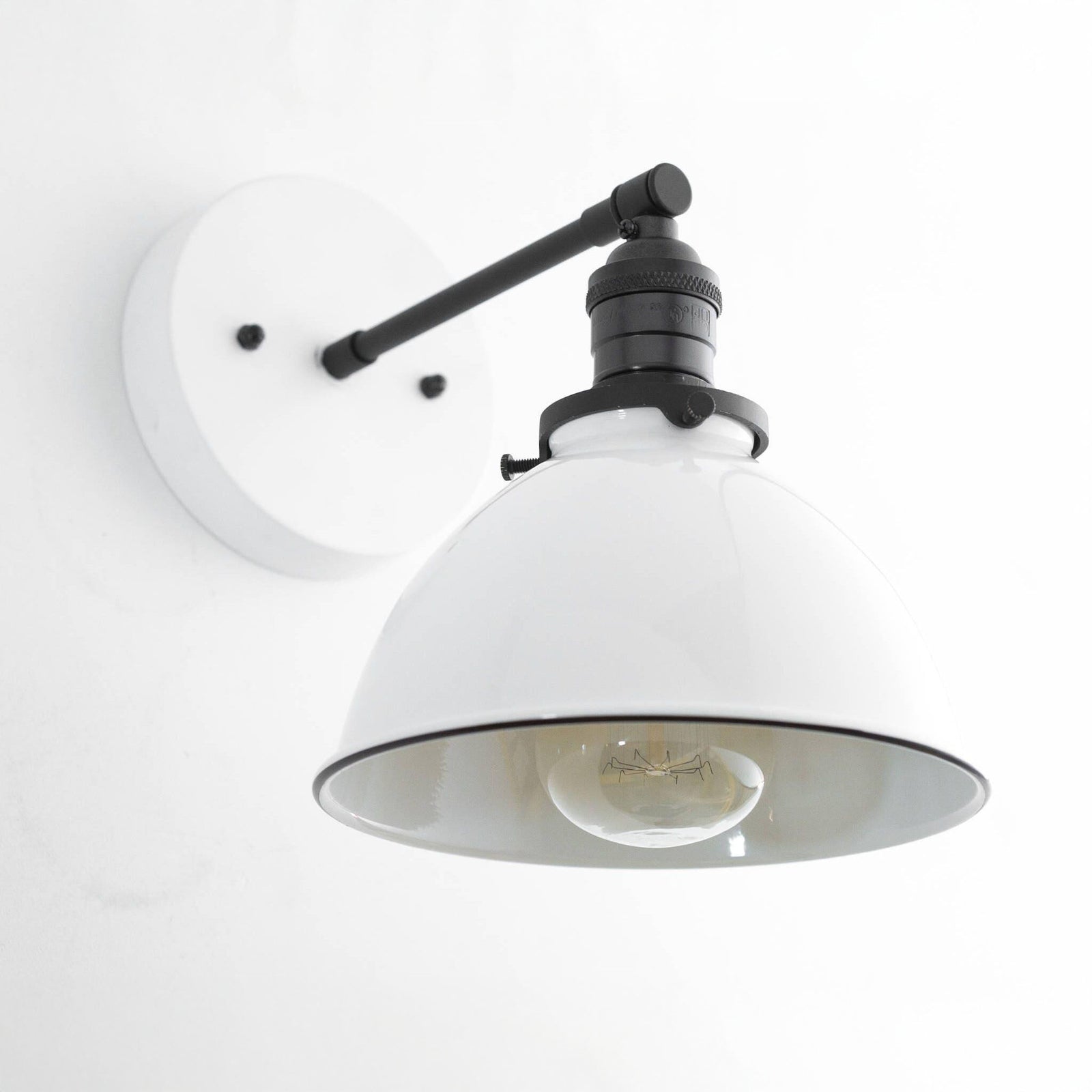 Sconce with a White round backplate and metal dome shade and a Black arm and socket over an exposed filament bulb. - SCONCE MODEL NO. 7026