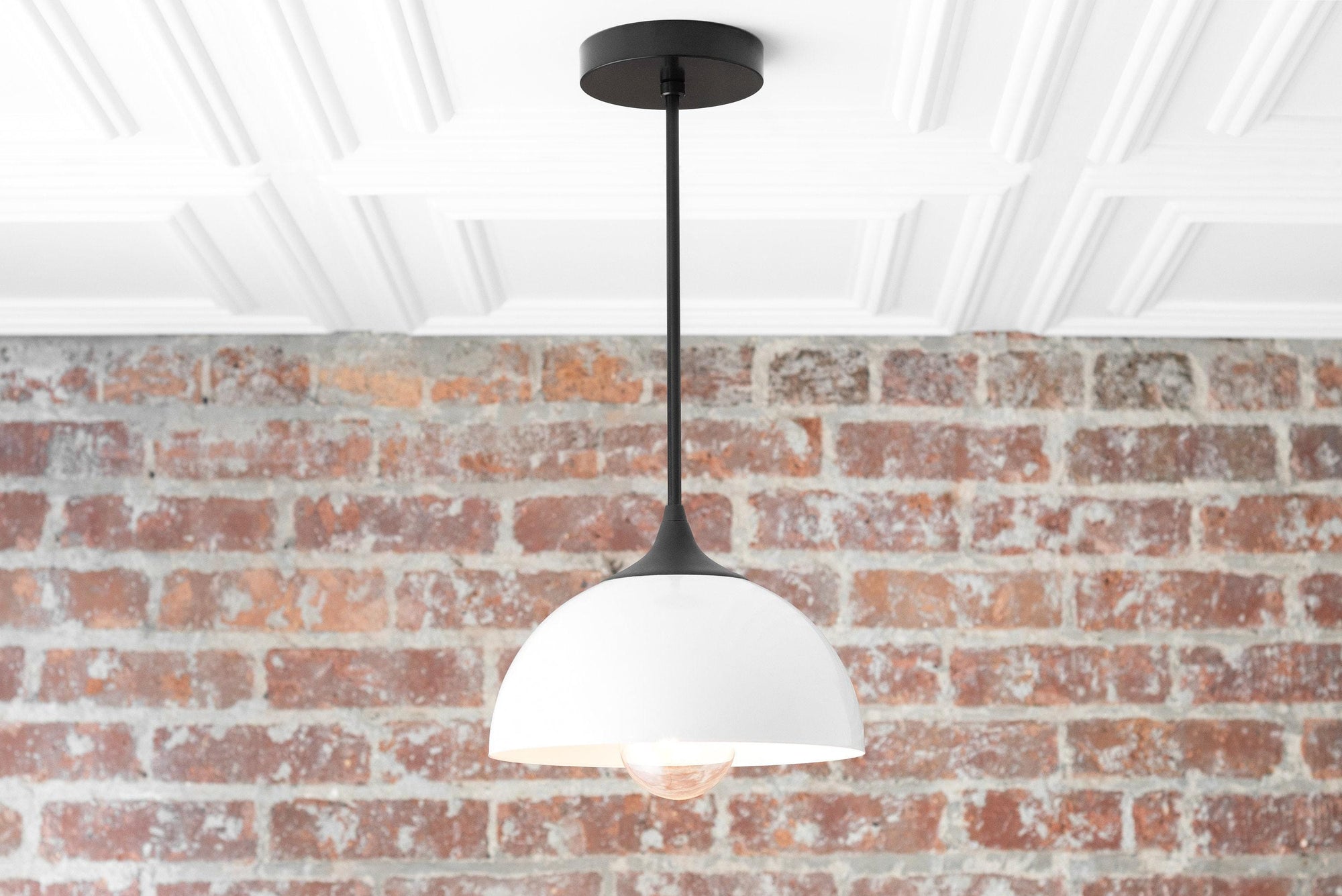 Mid-century modern pendant light with matte black fixture and white dome shade hanging against red brick wall. - PENDANT MODEL NO. 9263