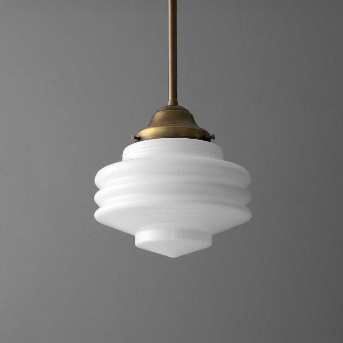 Pendant light with a tiered opal glass schoolhouse shade hanging from an Antique Brass stem and fitter. - PENDANT MODEL NO. 6071