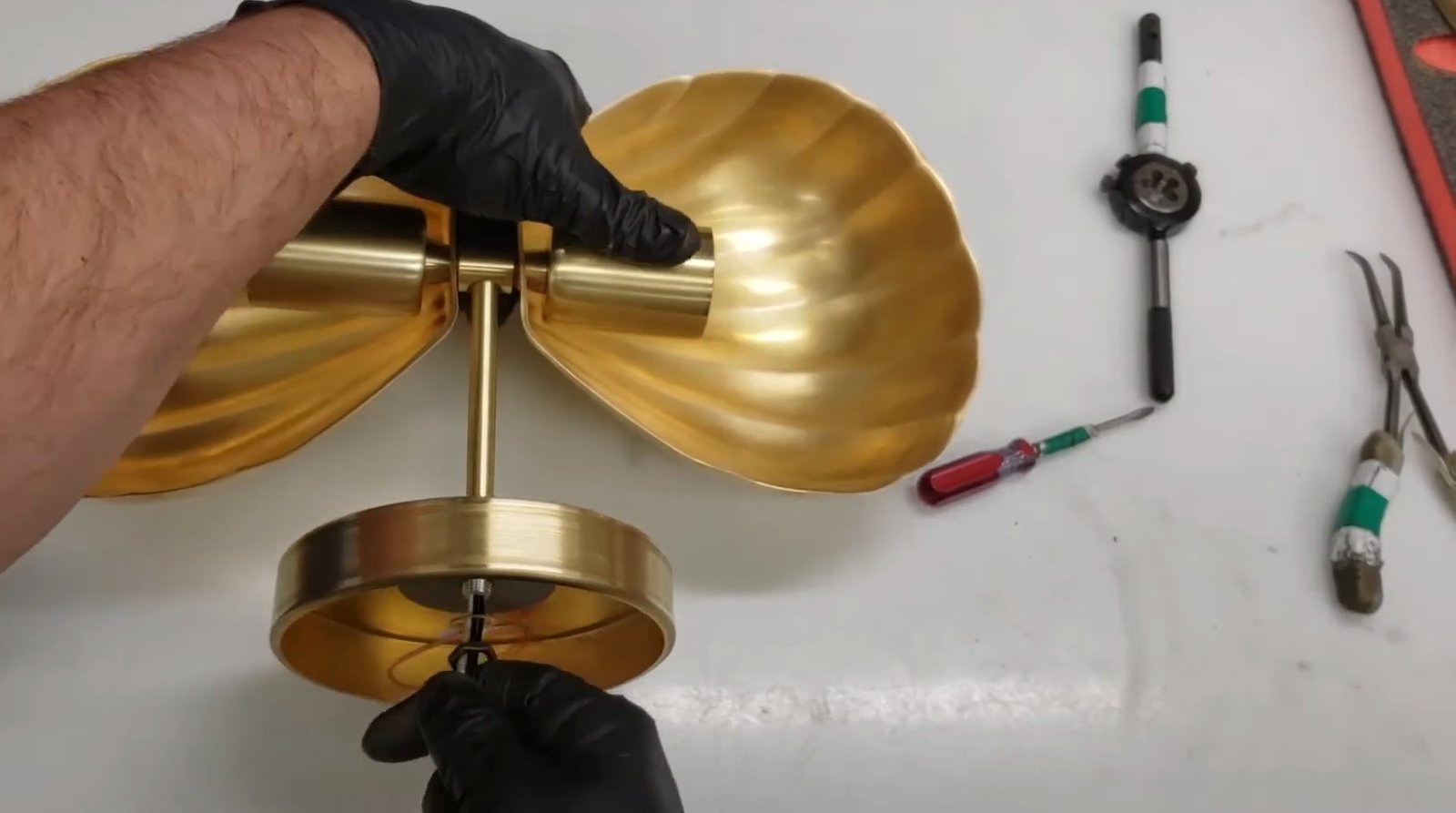 Gloved hands fitting the canopy of a twin fluted brass shell sconce on the workbench