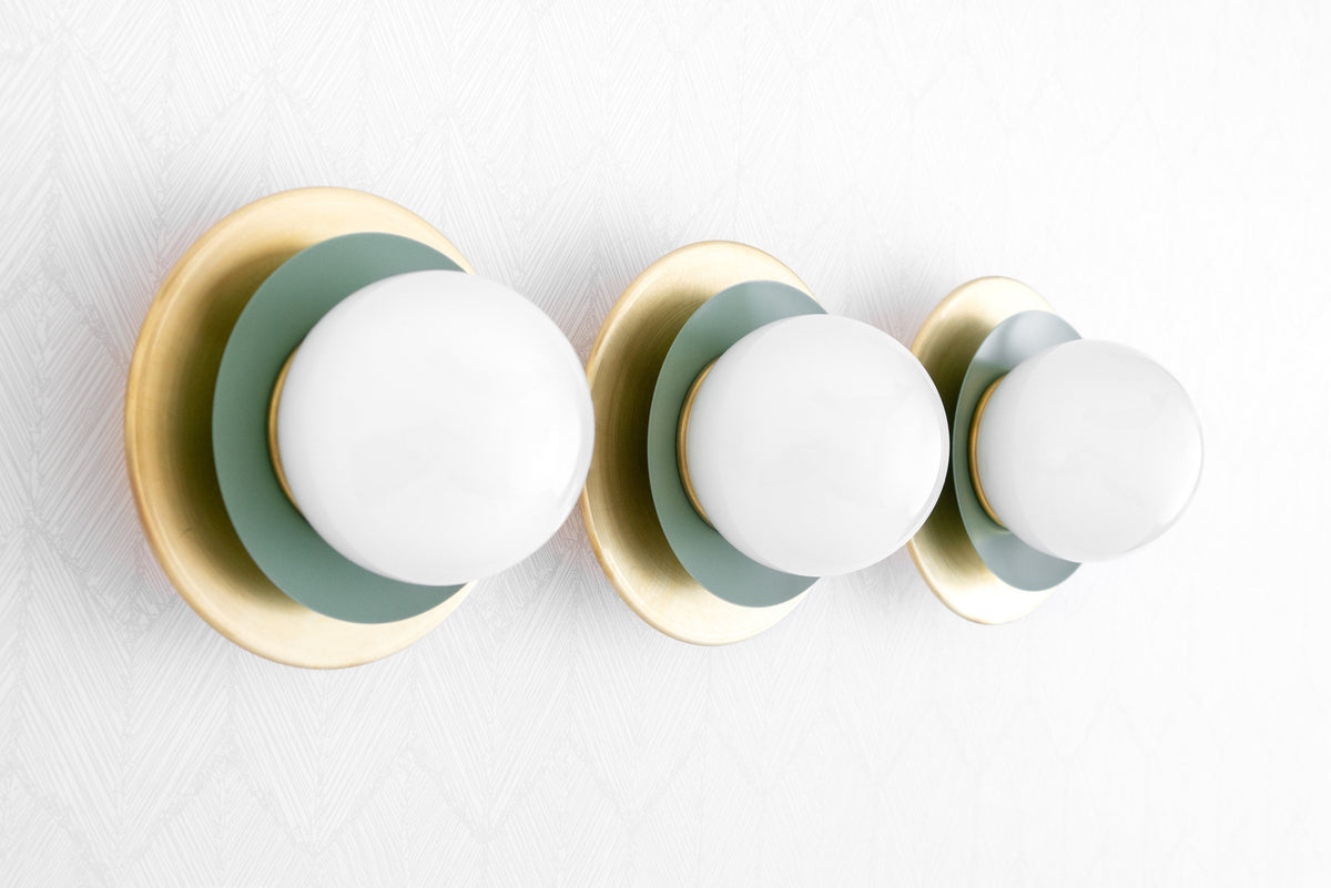 Mid-century modern vanity light with three white globe bulbs and raw brass with green circular backplates. - VANITY LIGHT MODEL NO. 7680
